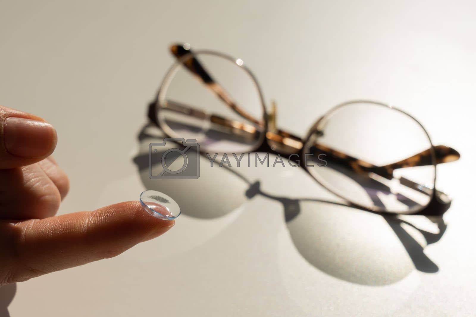 Royalty free image of Close-up of a contact lens on a female index finger against the background of glasses on a white table. by mrwed54