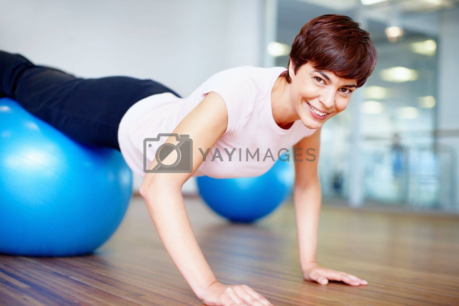 Royalty free image of Woman doing push ups on pilates ball. Portrait of woman doing push ups on pilates ball and smiling. by YuriArcurs