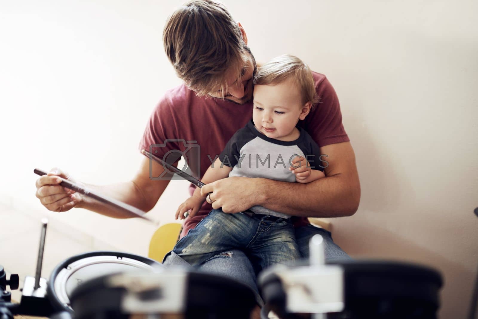 Royalty free image of Listen....can you hear it. A handsome young father teaching his young son to drum. by YuriArcurs