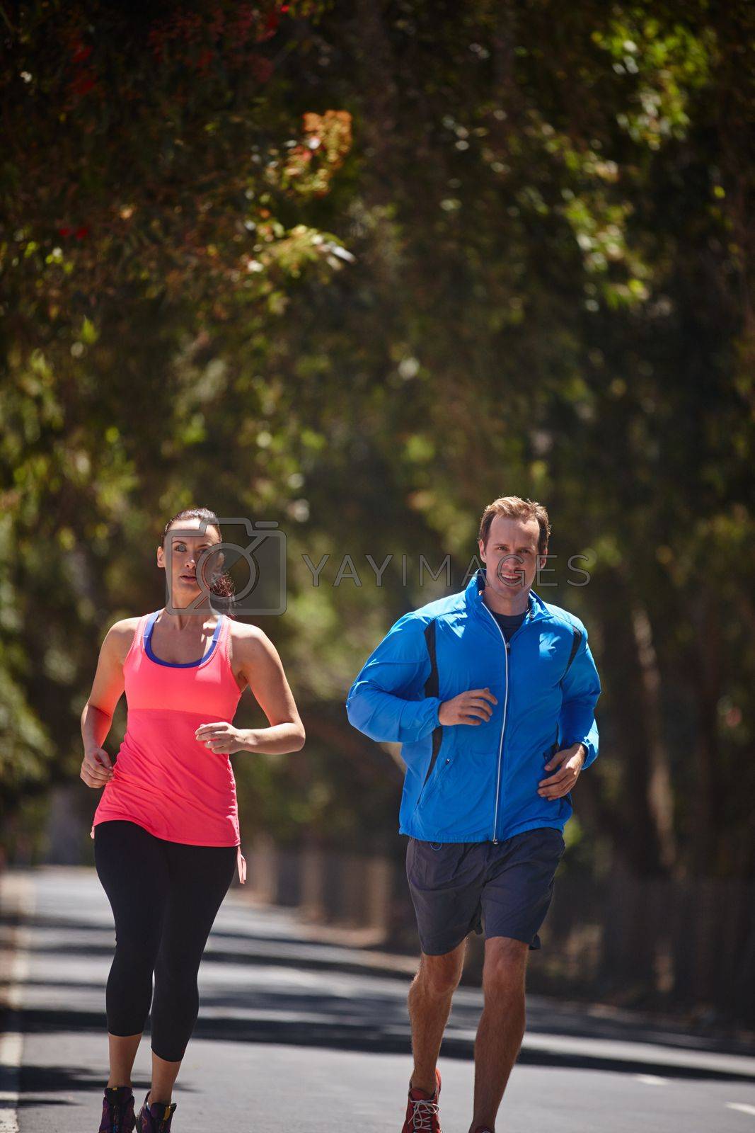 Royalty free image of The road to fitness is long but rewarding. a couple jogging on a road. by YuriArcurs