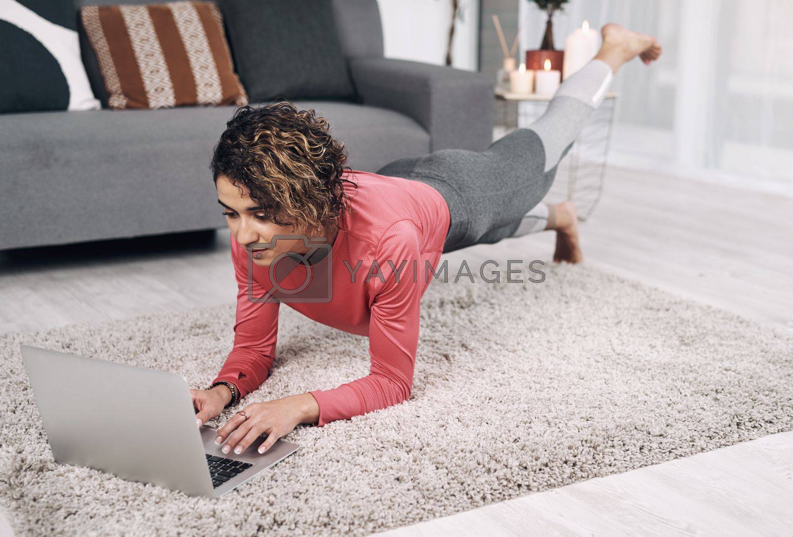Royalty free image of Yoga is a light, which once lit will never dim. an attractive young woman using a laptop while doing pilates on the lounge floor at home. by YuriArcurs