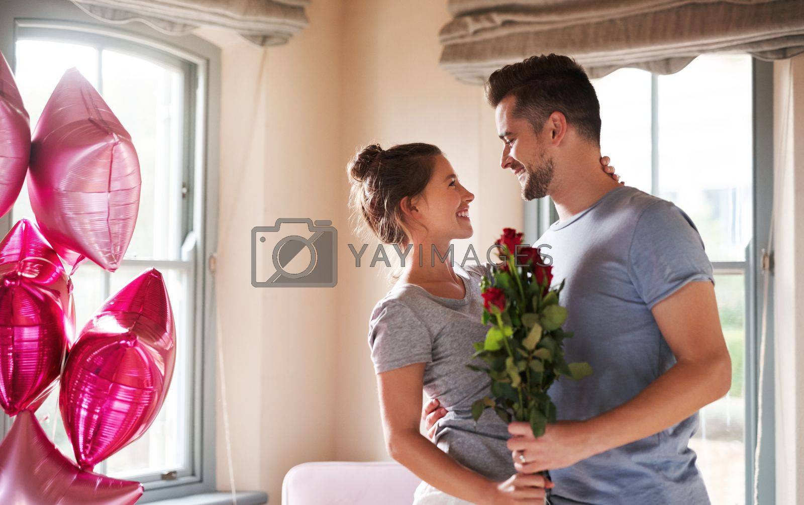 Royalty free image of Each day is a celebration of our love. a young man surprising his girlfriend with balloons and roses in their bedroom at home. by YuriArcurs