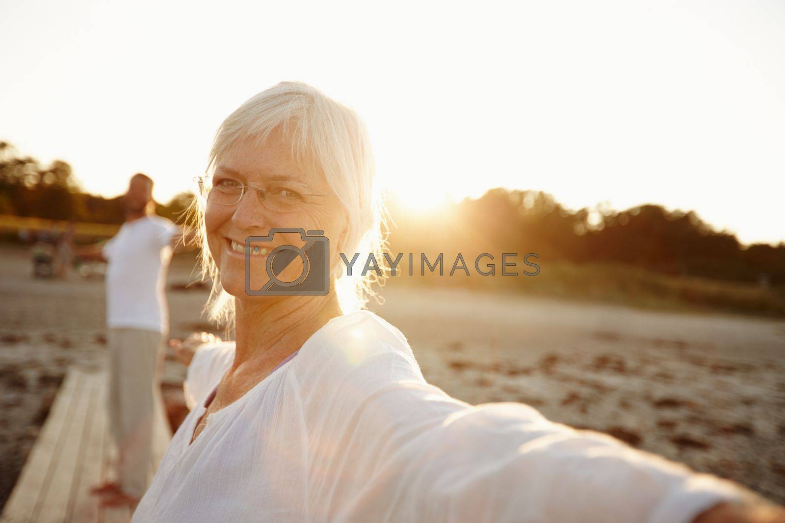 Royalty free image of Yoga makes me feel great. a mature woman doing yoga on the beach with her husband in the background. by YuriArcurs