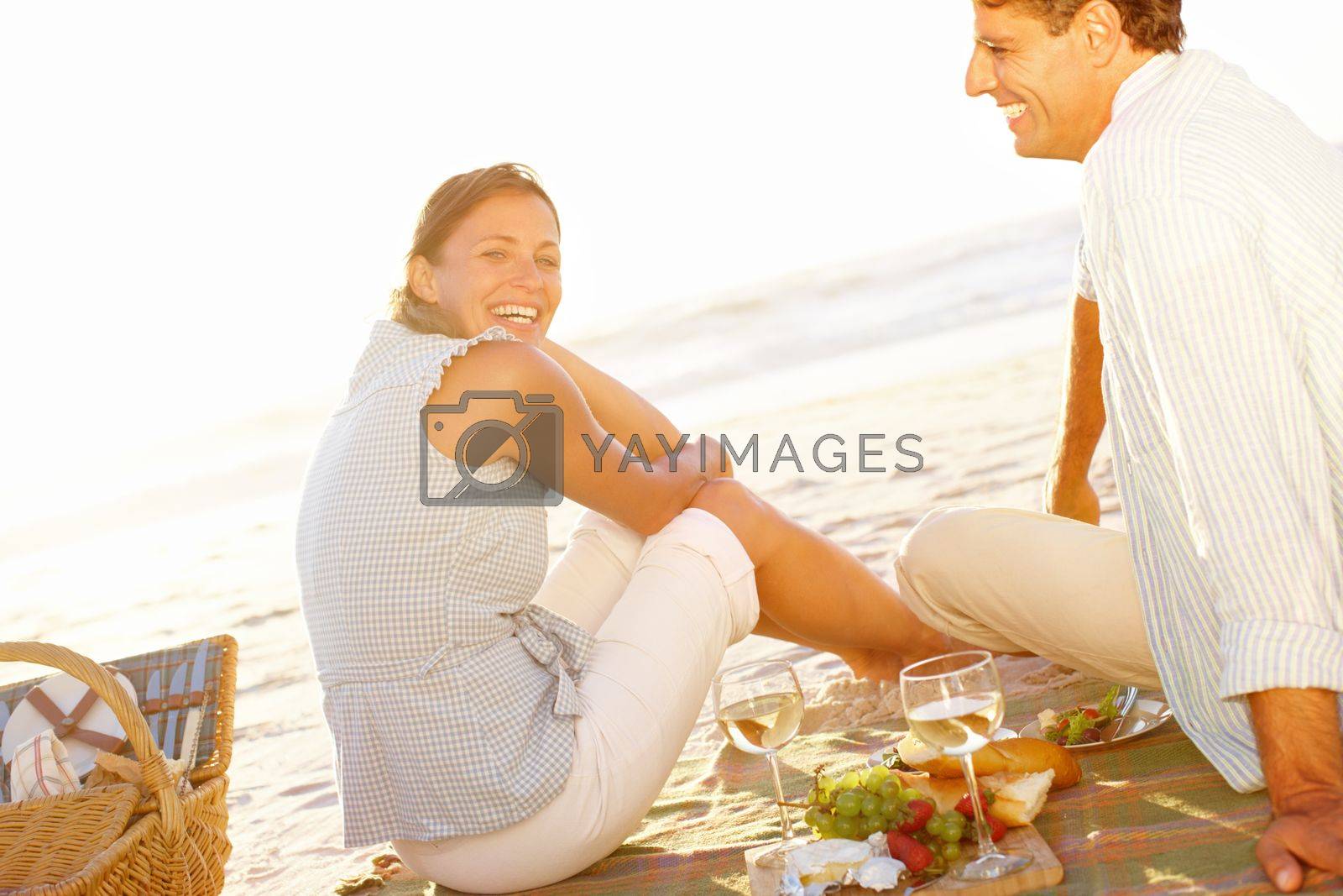 Royalty free image of Sunset and romance on the beach. Rear view of a mature couple enjoying a picnic on the beach during sunset. by YuriArcurs
