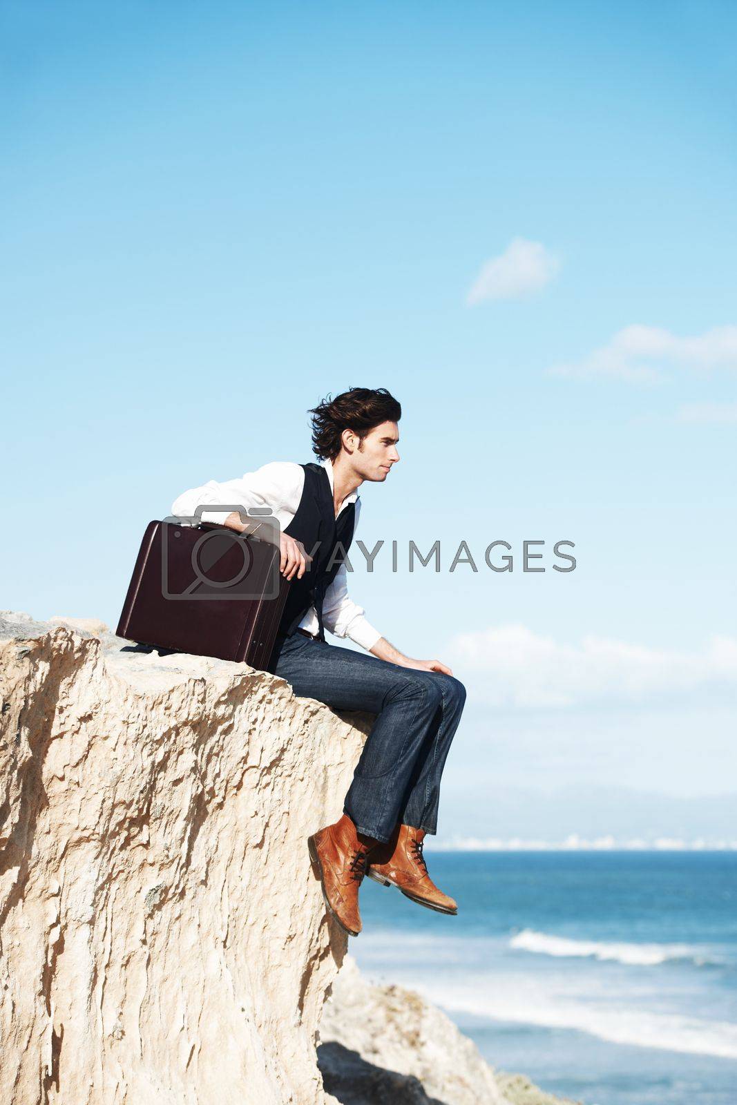 Royalty free image of Pondering the meaning of life. Pensive young man sitting with his briefcase on the edge of a cliff overlooking the ocean. by YuriArcurs