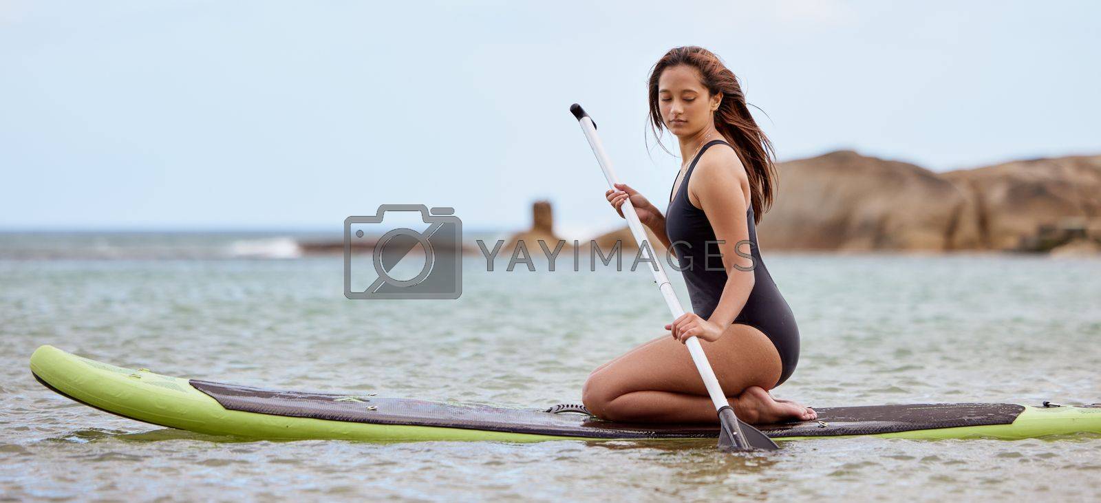 Surfer, fitness and woman in ocean with surfboard and paddle, swimwear and focus with sport outdoor and nature. Beach, exercise and young female surfing, waves and adventure with extreme sports.