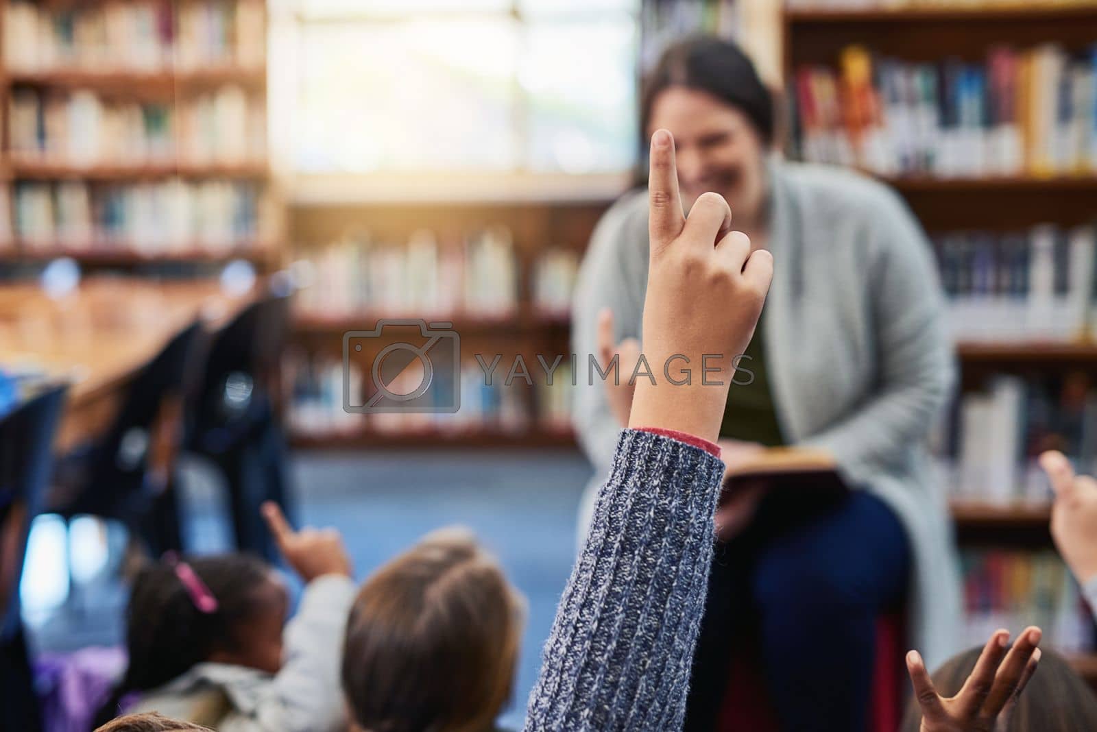 Royalty free image of Kids have many questions that fuel their curious minds. an elementary school boy raising his hand to his teacher in the library. by YuriArcurs
