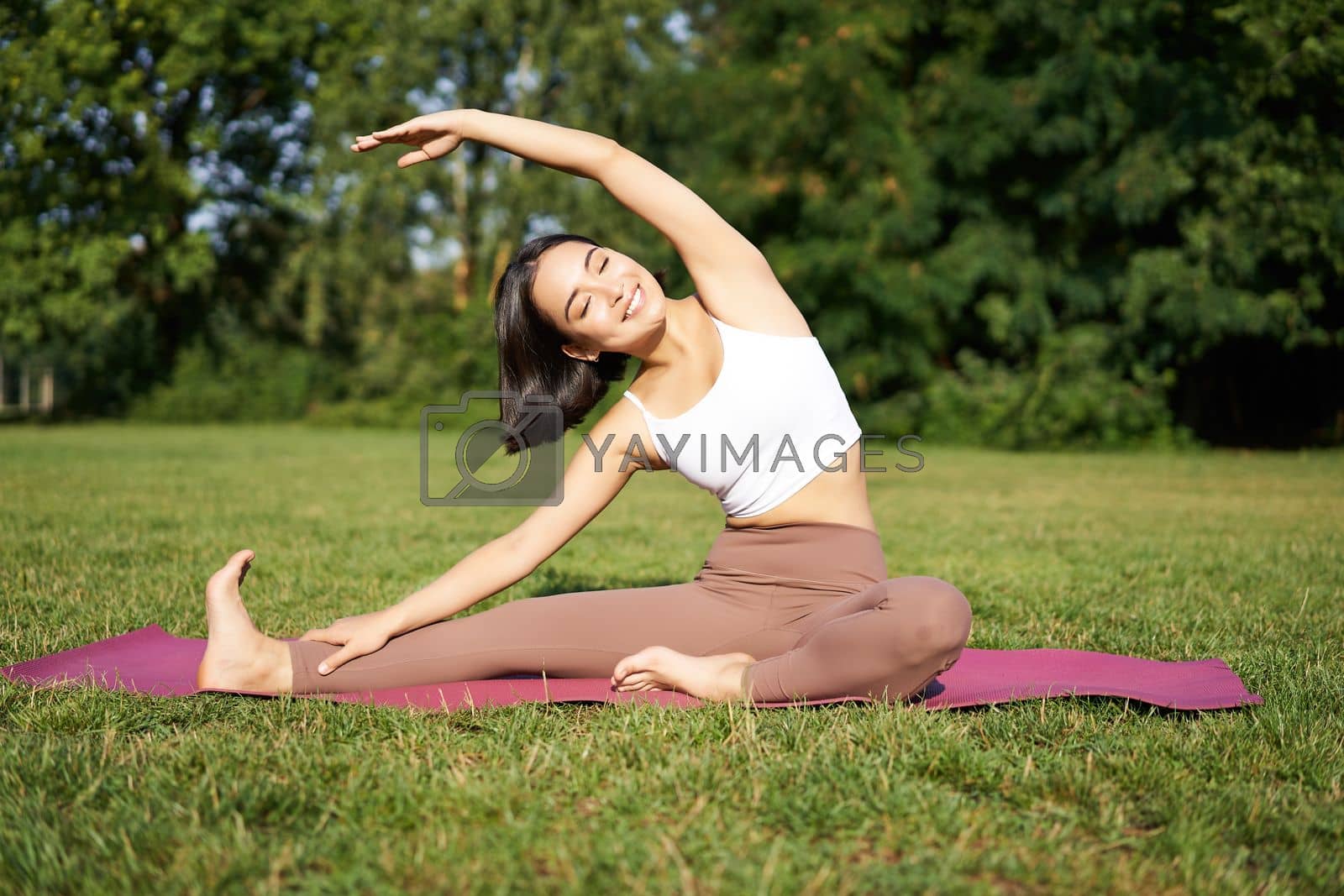 Royalty free image of Young woman does yoga on lawn in park, stretching on fitness mat, wellbeing concept by Benzoix