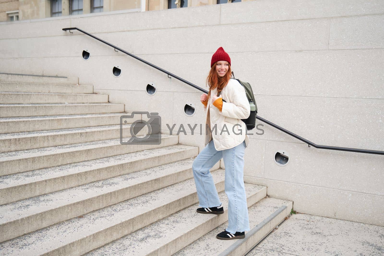 Royalty free image of Young stylish girl traveller goes sightseeing, travels around city with backpack, tourist smiles and looks around by Benzoix