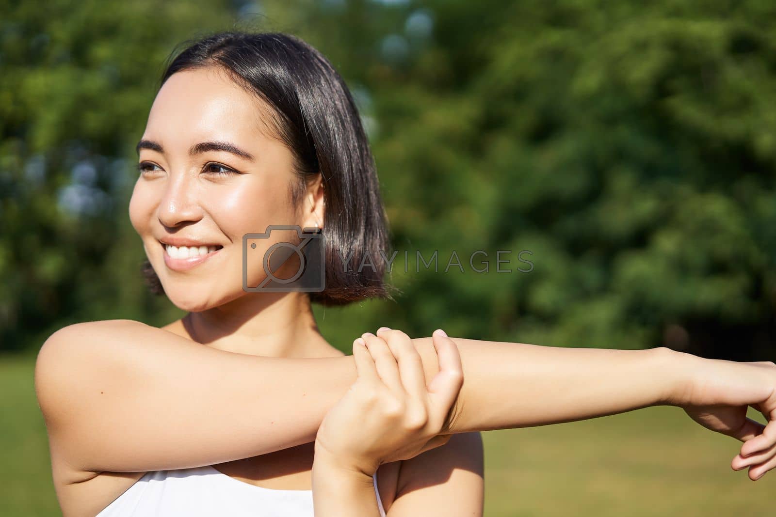 Royalty free image of Portrait of young fitness woman stretching her arms, warm-up before training session, sport event in park, jogging and excercising by Benzoix