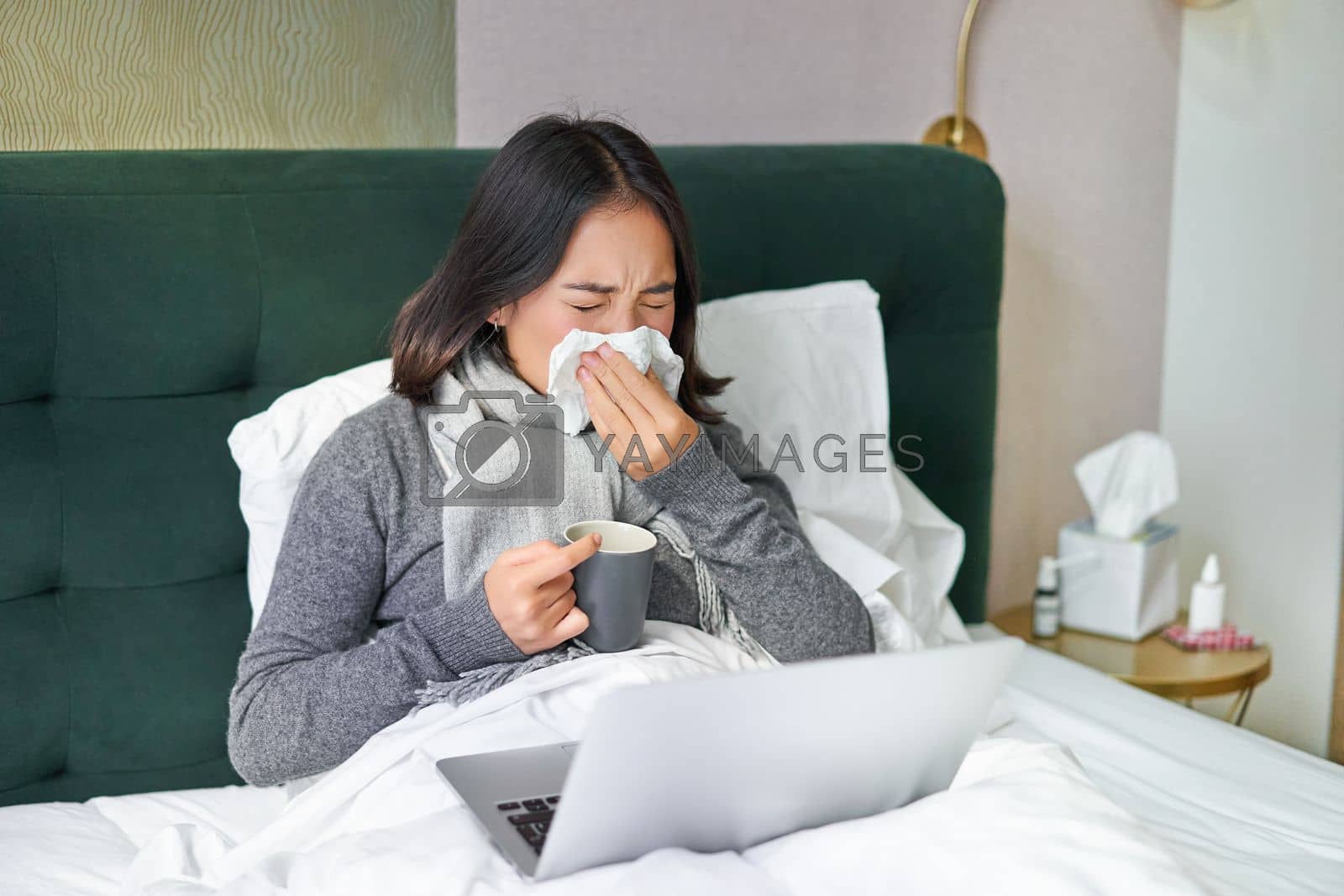Royalty free image of Woman with cold, having flu, staying in bed, sneezing in napkin, runny nose and influenza symptoms by Benzoix