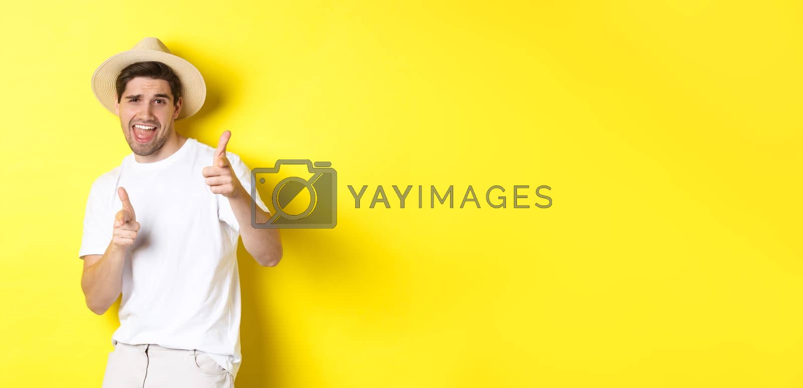 Royalty free image of Concept of tourism and vacation. Happy cool guy pointing fingers at you, standing over yellow background by Benzoix