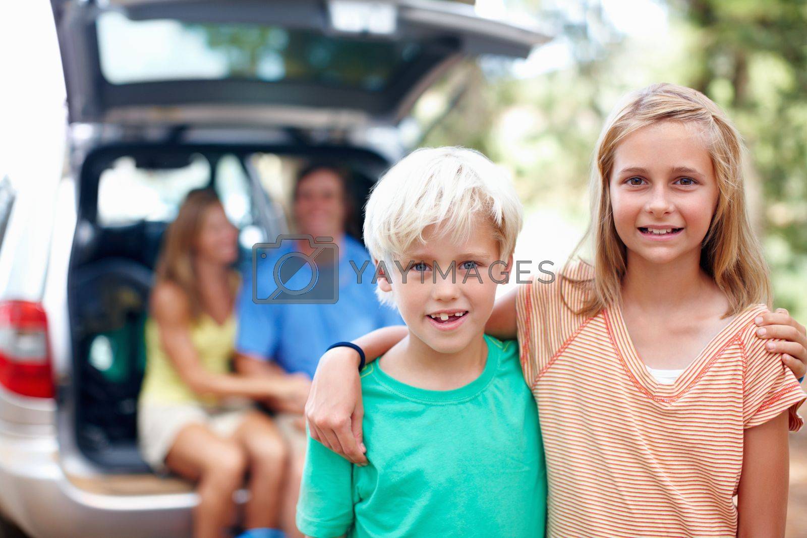 Royalty free image of Brother and sister standing with arms around and smiling. Brother and sister standing with arms around and parents sitting in the back of a car. by YuriArcurs