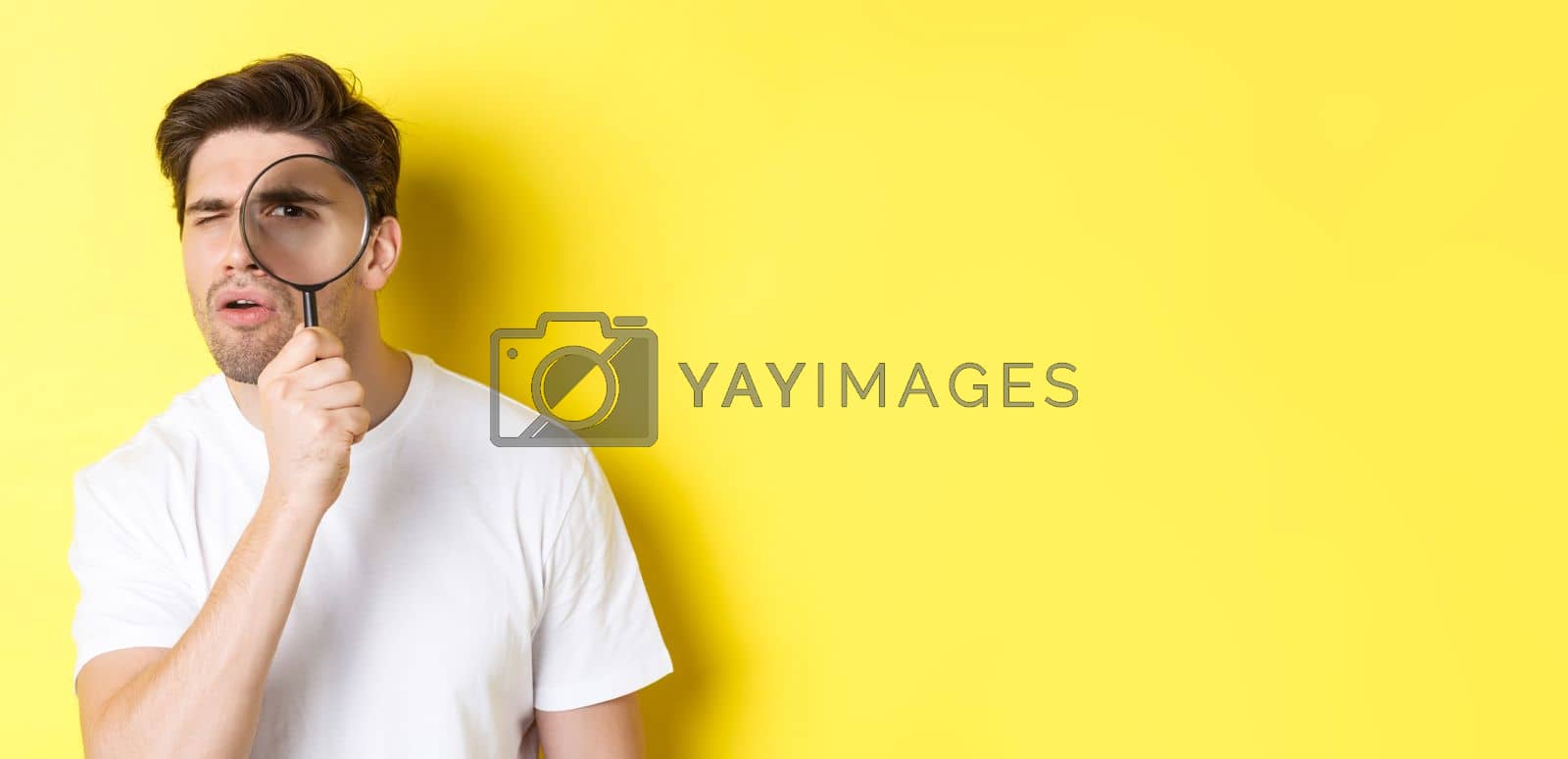 Royalty free image of Man looking through magnifying glass with serious and thoughtful look, searching or investigating, standing over yellow background by Benzoix