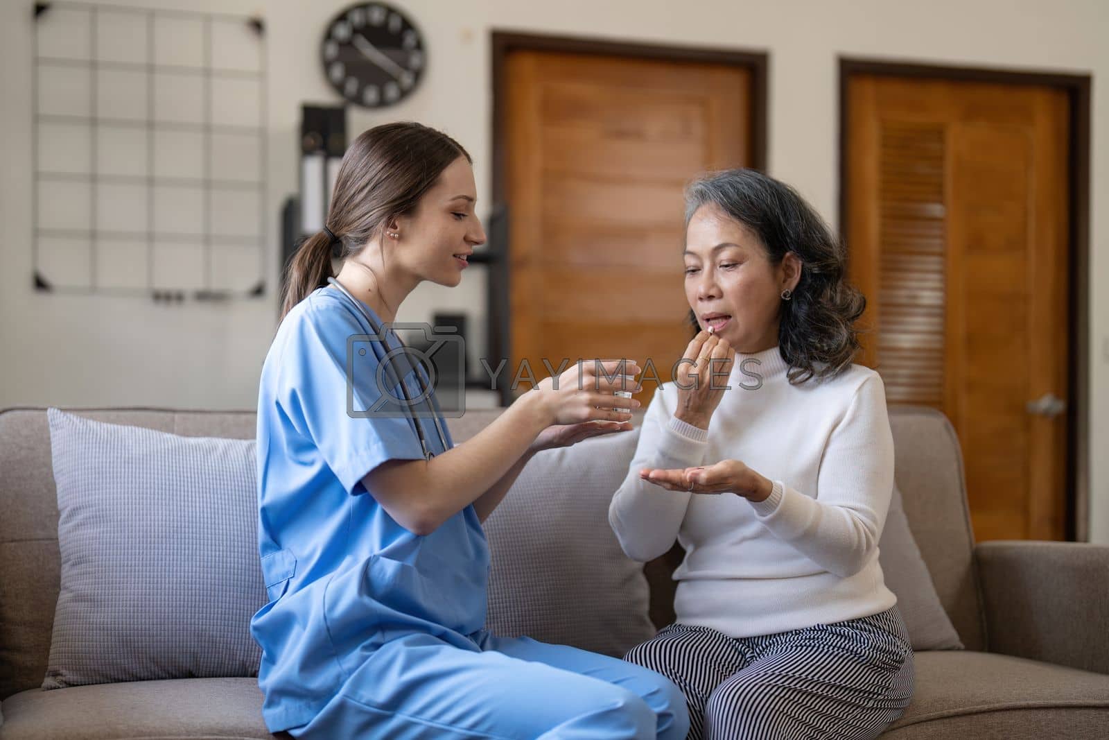 Royalty free image of Contented senior woman taking medicines while her caregiver advising her medication. Medication for seniors, nursing house, healthcare at home by nateemee
