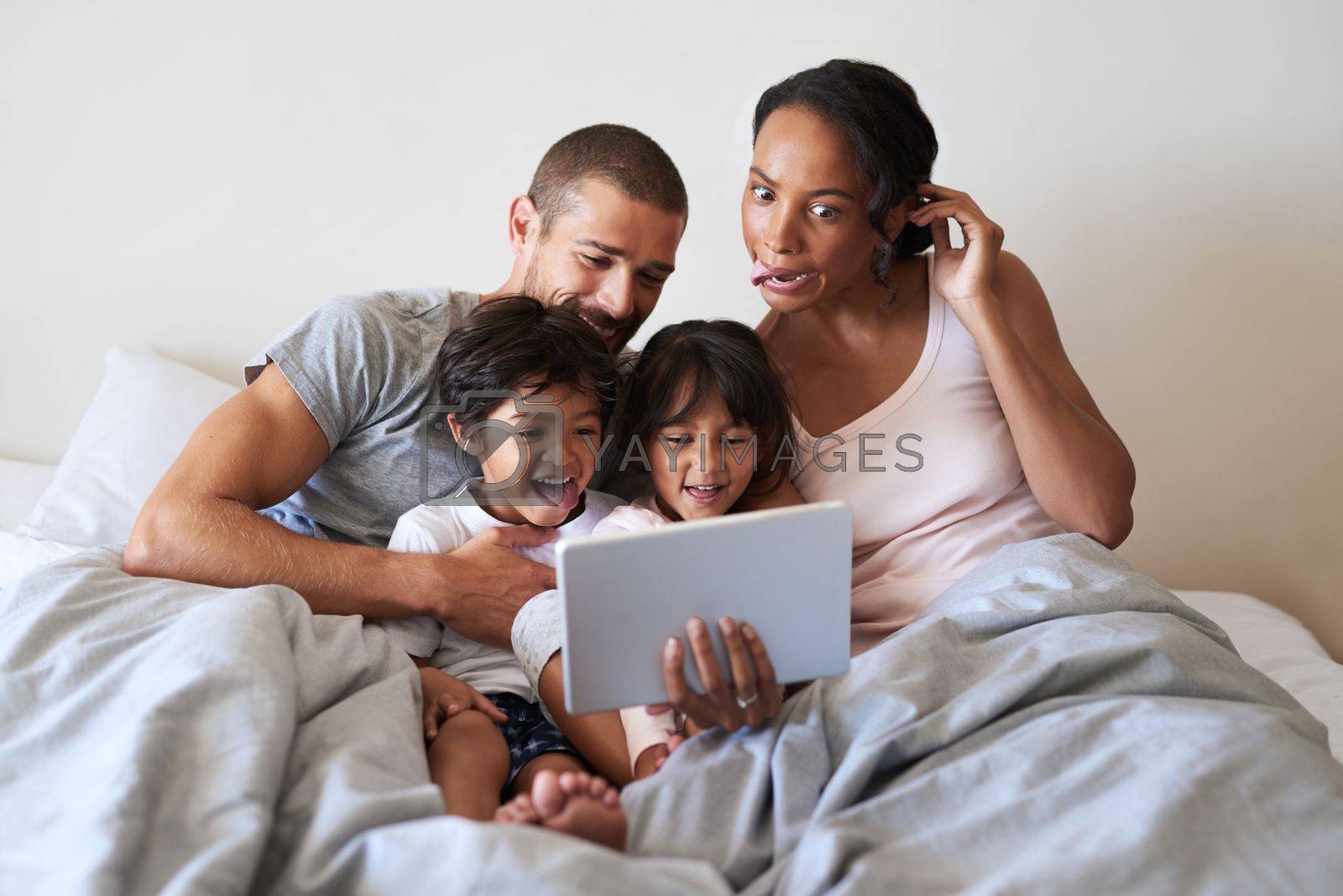 Royalty free image of We get a little crazy when were all together. a beautiful young family of four taking selfies with a digital tablet in their bedroom. by YuriArcurs