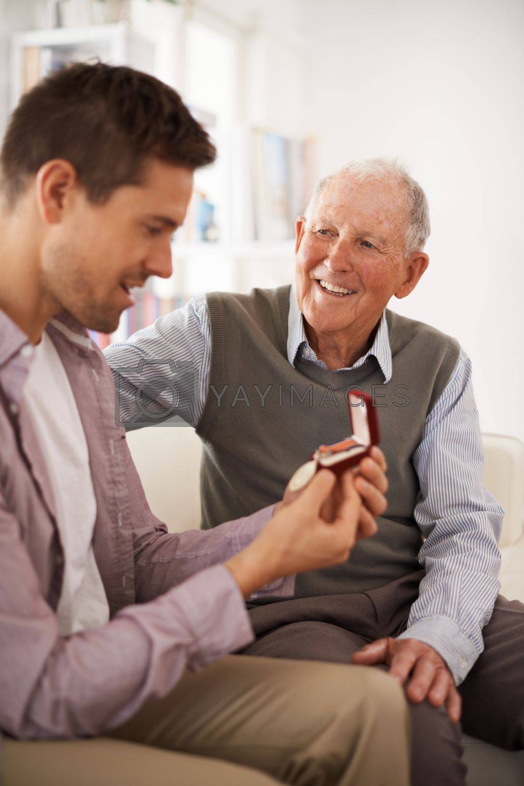 Royalty free image of The family heirloom. a senior father giving his son a medal as theyre sitting indoors. by YuriArcurs