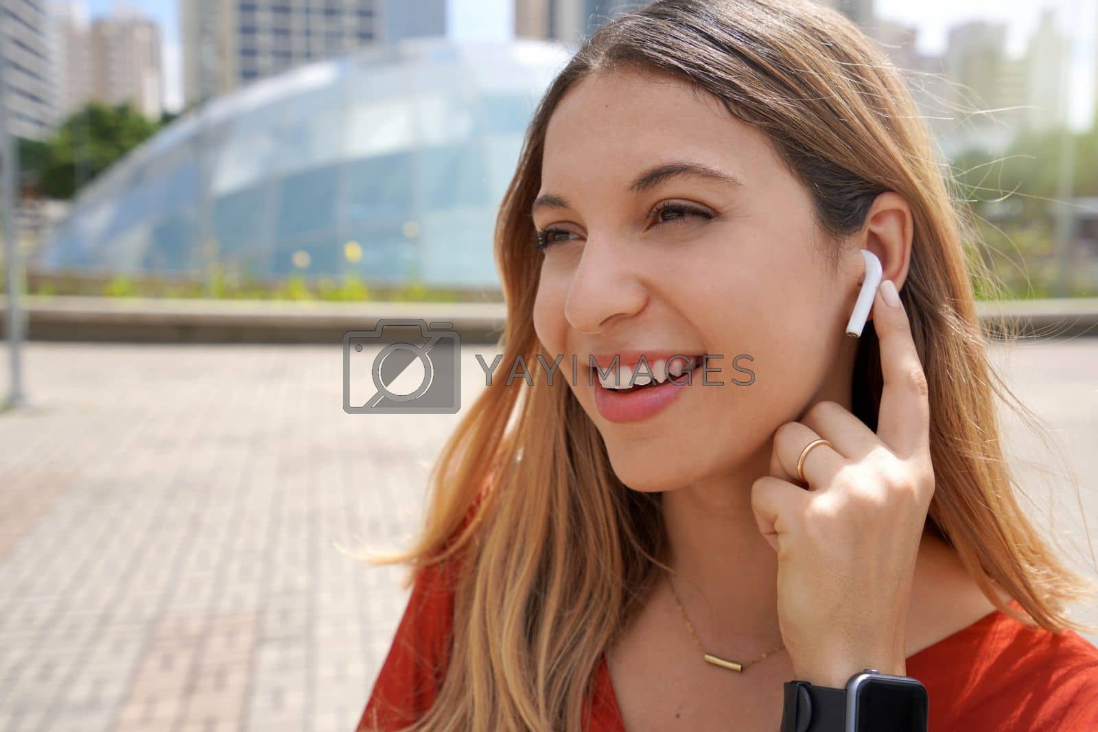 Royalty free image of Close-up of laughing girl connecting her wireless earphones with finger in Sao Paulo modern metropolis by sergio_monti