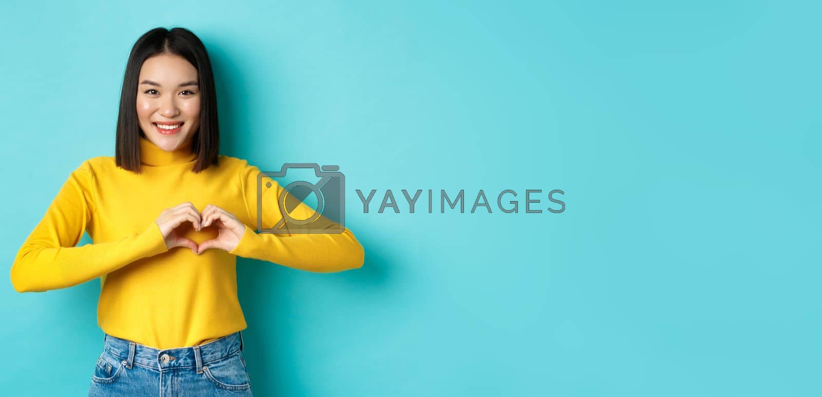 Royalty free image of Valentines day and romance concept. Beautiful asian woman show I love you, heart gesture and smiling, standing against blue background by Benzoix
