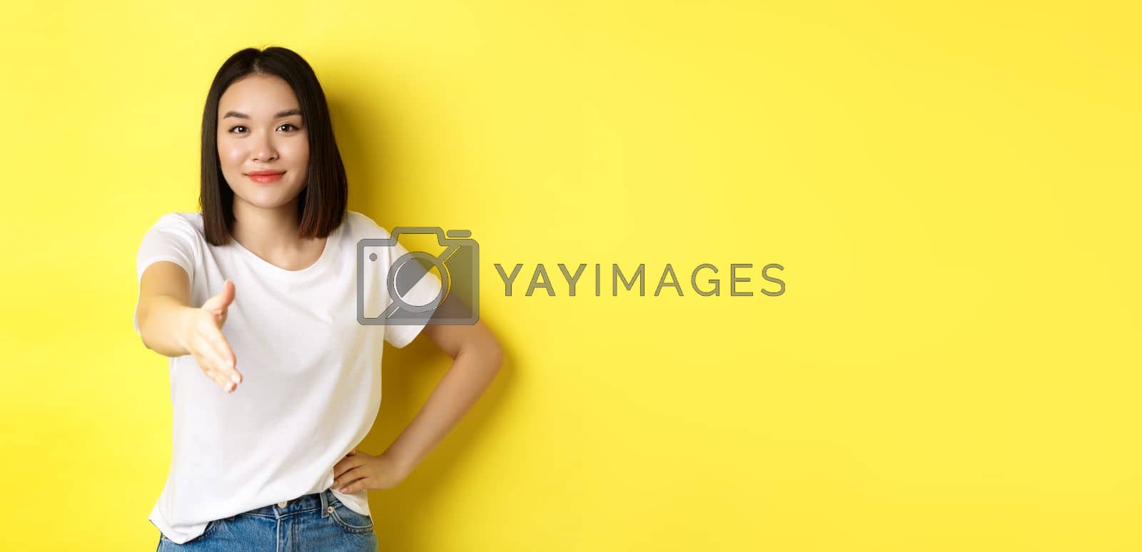 Royalty free image of Confident asian woman in white t-shirt, stretch out hand for handshake and greeting gesture, saying hello, introduce herself, standing over yellow background by Benzoix