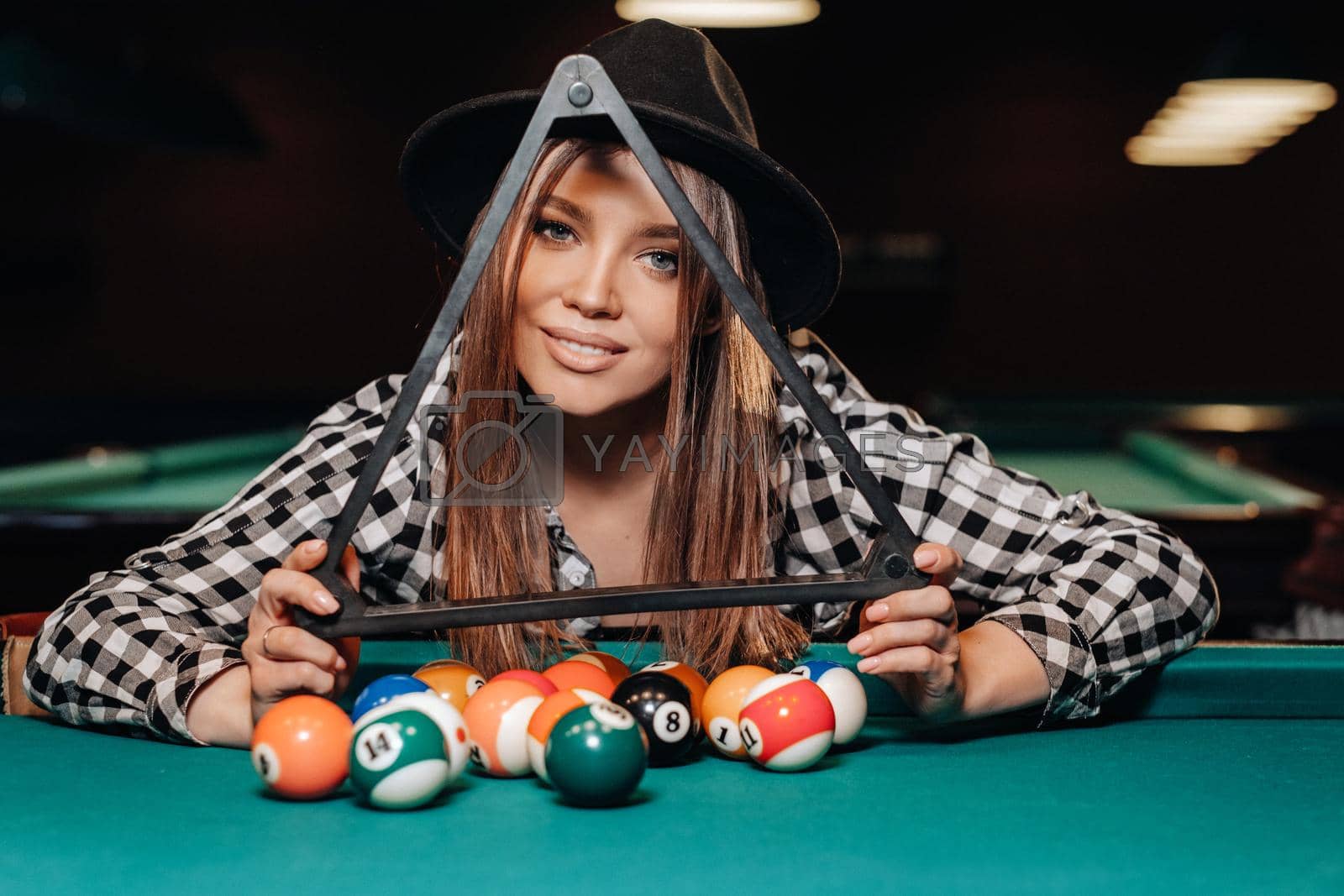 Royalty free image of A girl in a hat in a billiard club with balls in her hands.Playing billiards by Lobachad
