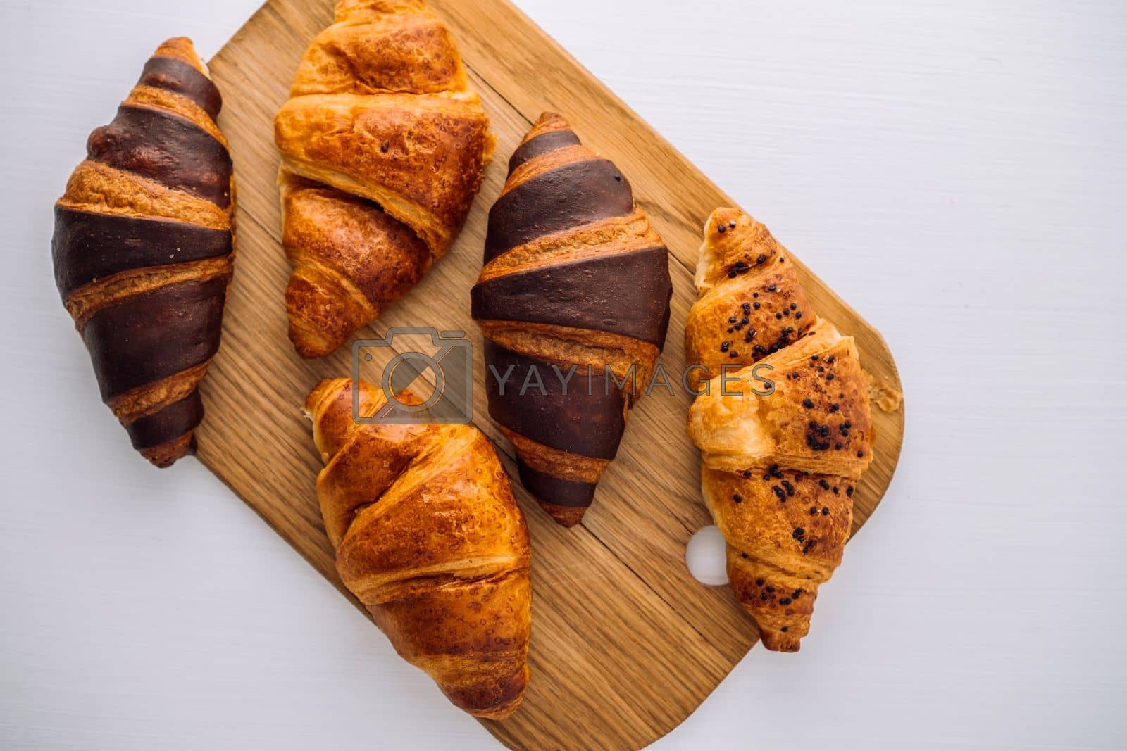 Royalty free image of Flat lay of bunch of appetizing brown and chocolate croissants on a wooden board on white table by Romvy