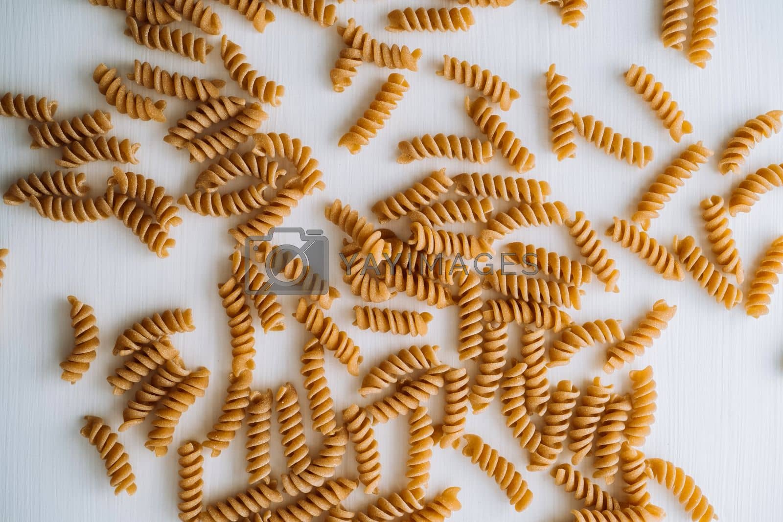 Royalty free image of Flat lay of scattered many wavy pasta from whole wheat flour on white table by Romvy