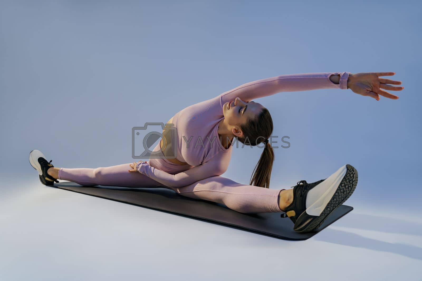 Royalty free image of Flexible woman doing stretching exercises on yoga mat on studio background. Healthy lifestyle by Yaroslav_astakhov