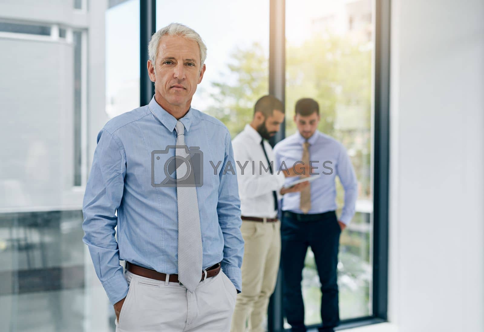 Royalty free image of We share the same ambitious drive. Portrait of a mature businessman standing in an office with colleagues in the background. by YuriArcurs