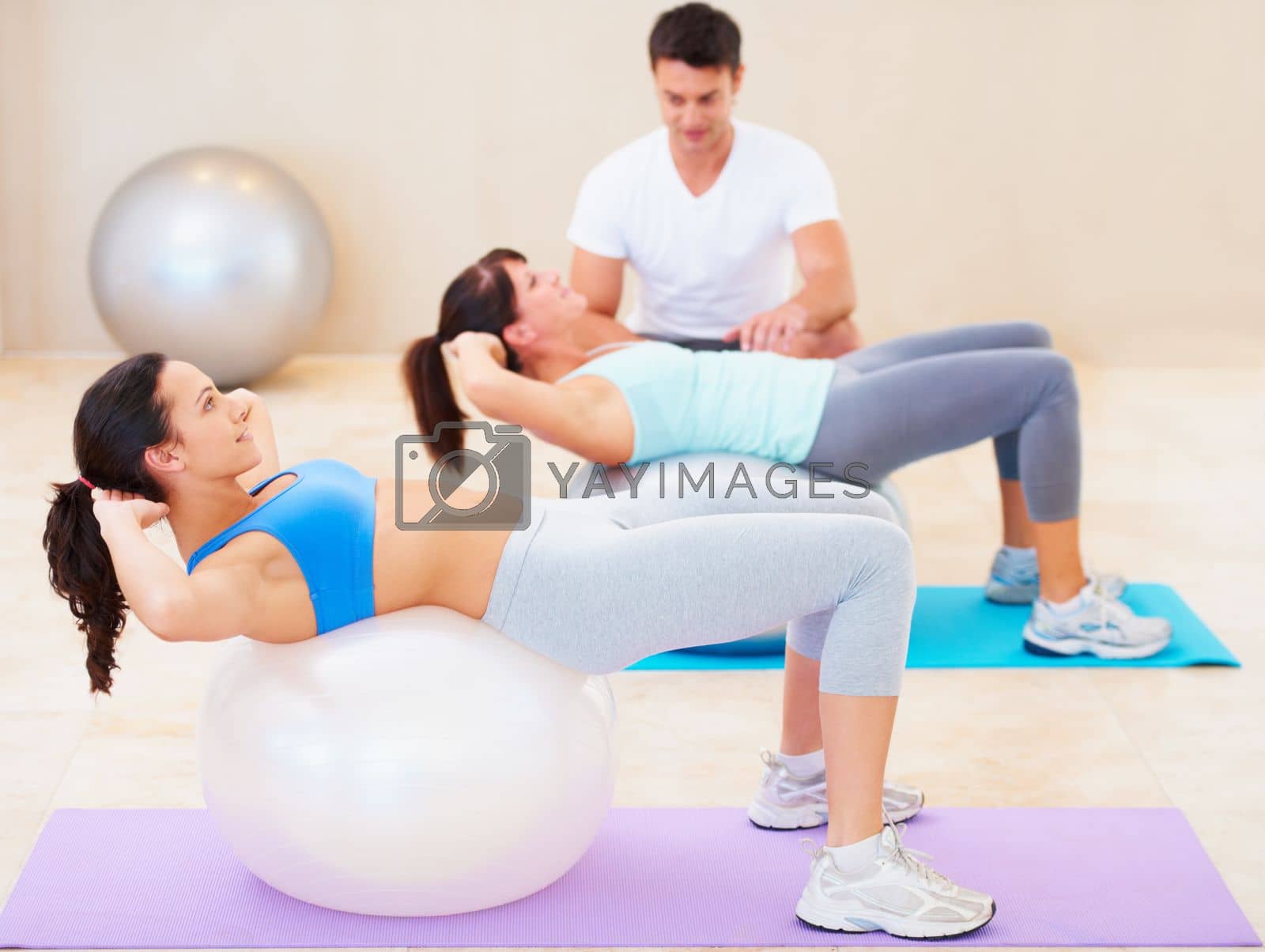 Royalty free image of Safe sit-ups for weak backs. Young woman doing a sit up during a pilates class with the help of an instructor. by YuriArcurs