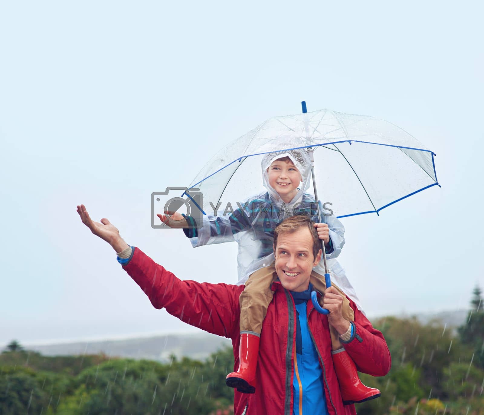 The weather wont spoil our fun. a father carrying his son on his shoulders outside in the rain