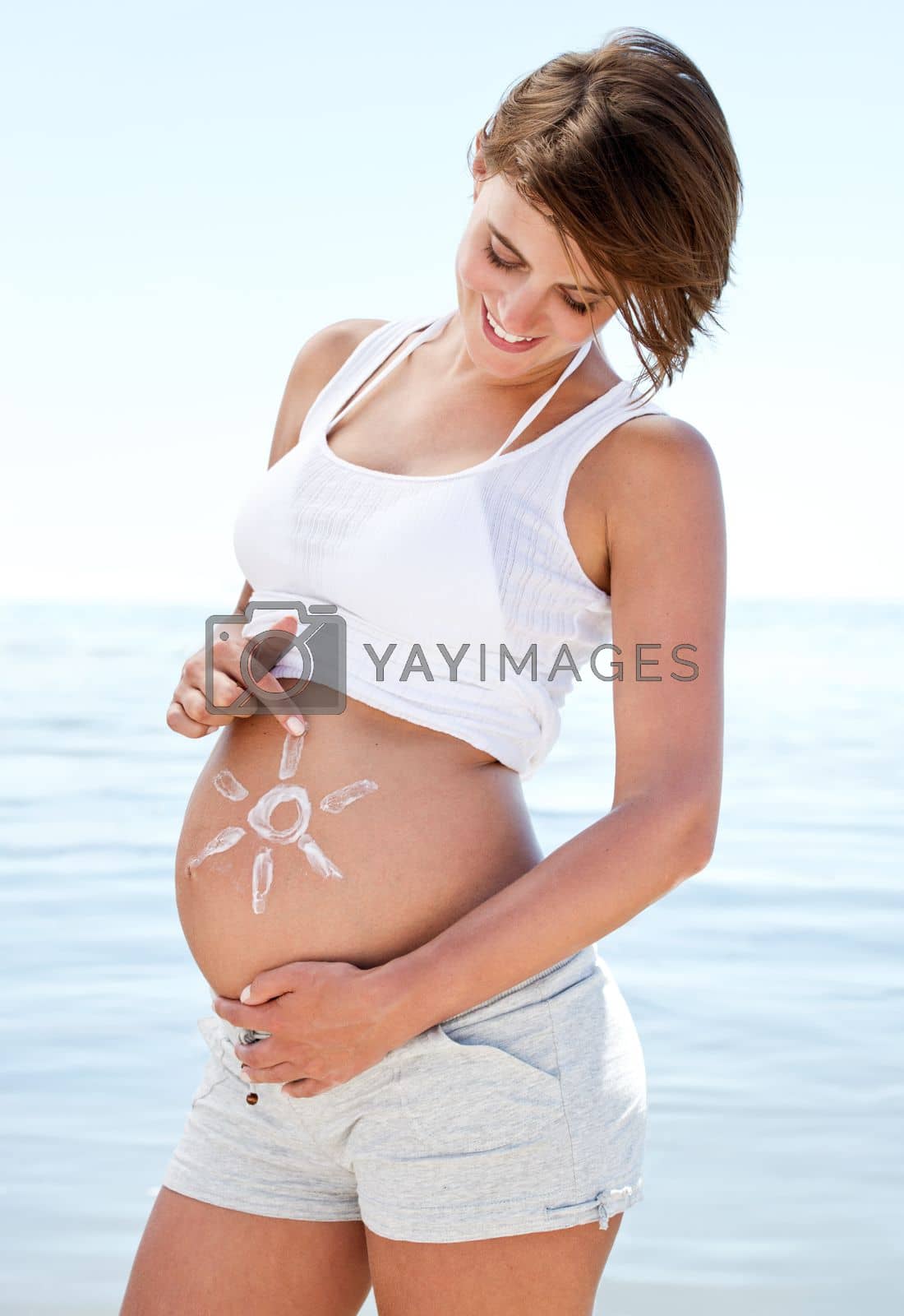 Royalty free image of My little ray of sunshine. a beautiful pregnant woman with the sun drawn onto her belly against the background of the ocean. by YuriArcurs