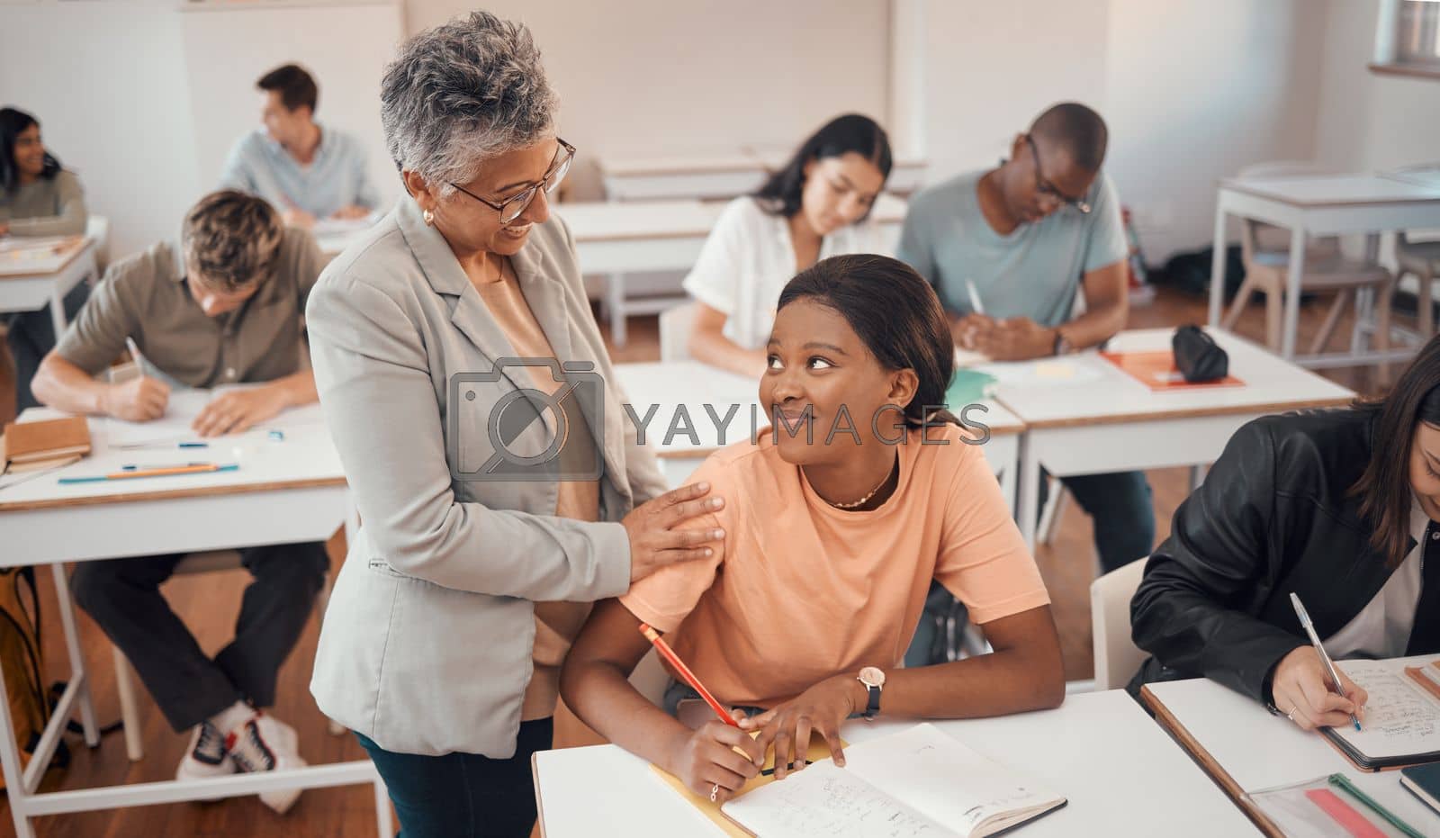 Royalty free image of Teacher, student and classroom for test, knowledge and learning for higher education. Young female, black woman or educator helping pupil in exams, talking or students writing notes in books or focus by YuriArcurs