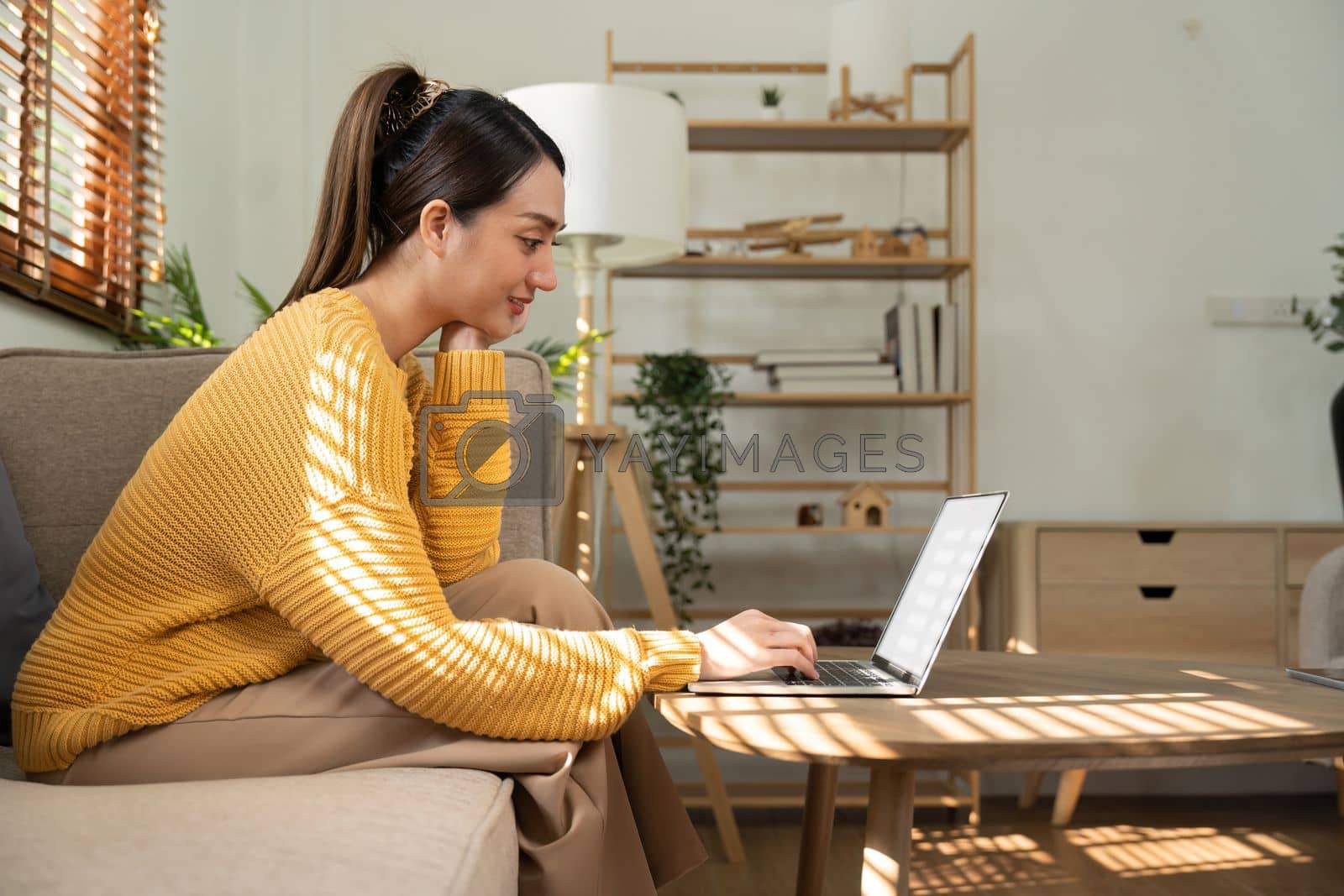 Royalty free image of Happy Asian woman while using her laptop in the living room. work from home by nateemee