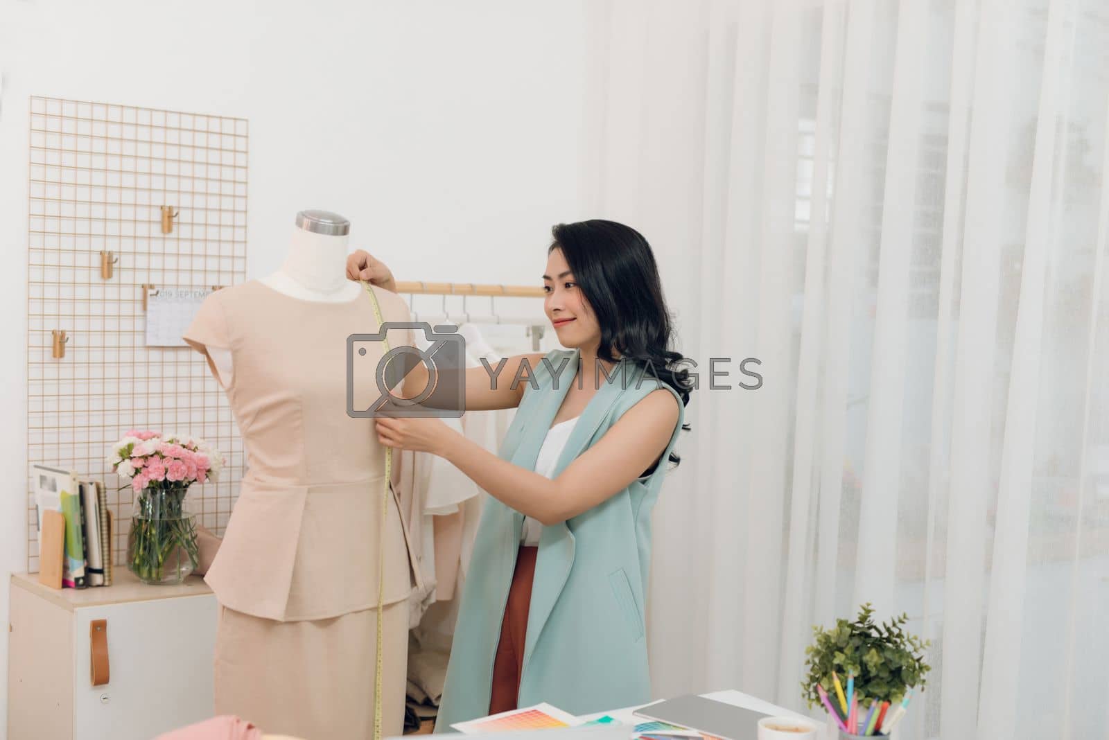 Royalty free image of Young Asian female fashion designer taking measurements on mannequin in her studio by makidotvn