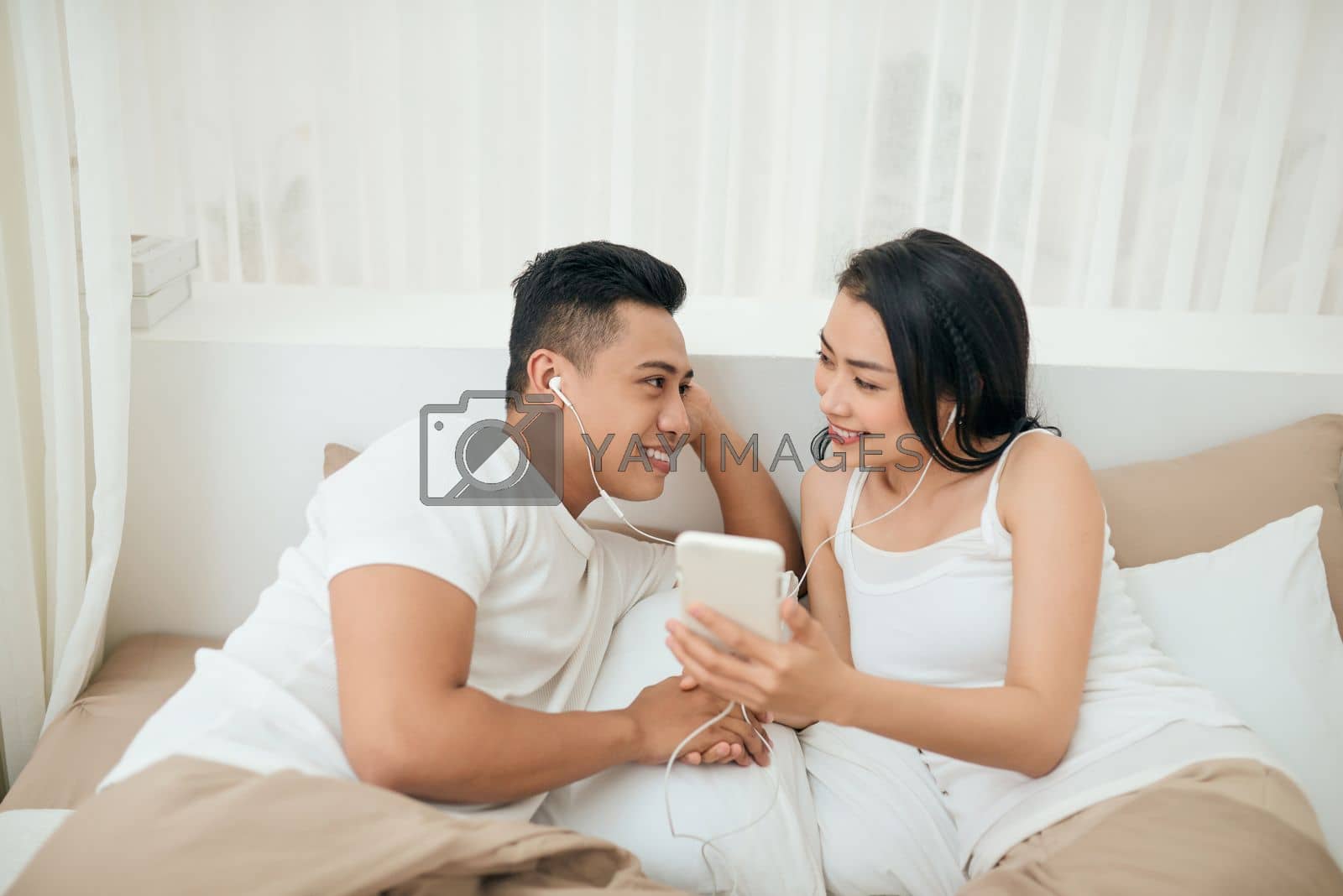 Royalty free image of Young asian couple smile listen music with smart mobile phone on bed at bedroom with fun and enjoy by makidotvn