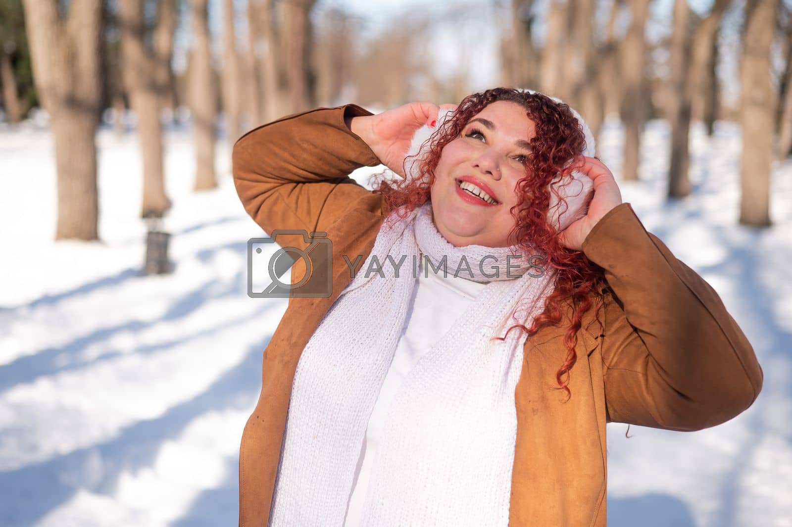 Royalty free image of Cheerful fat caucasian woman in fur headphones outdoors. by mrwed54