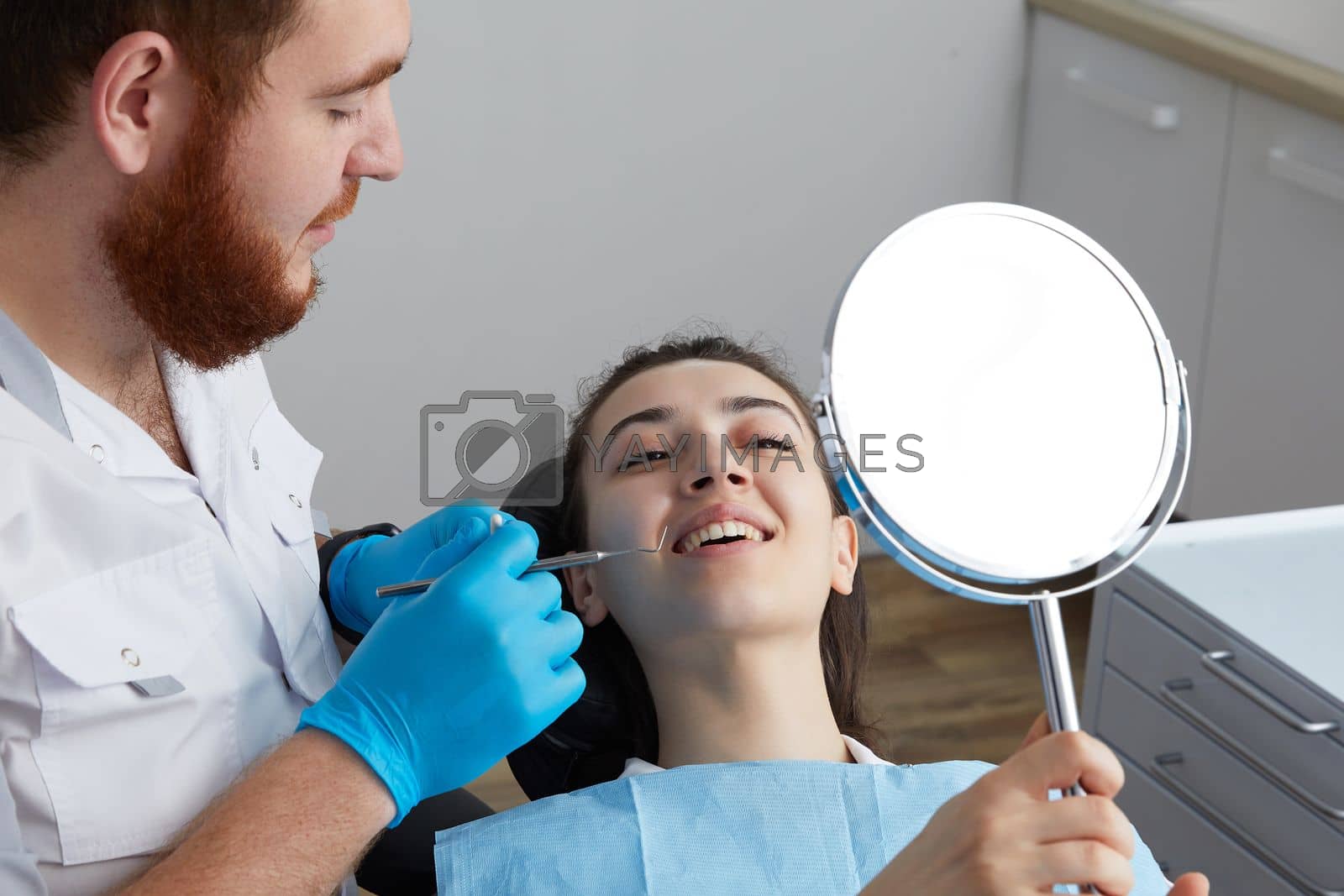 Royalty free image of Young Woman checking her beautiful smile in mirror after stomatological treatment by Mariakray
