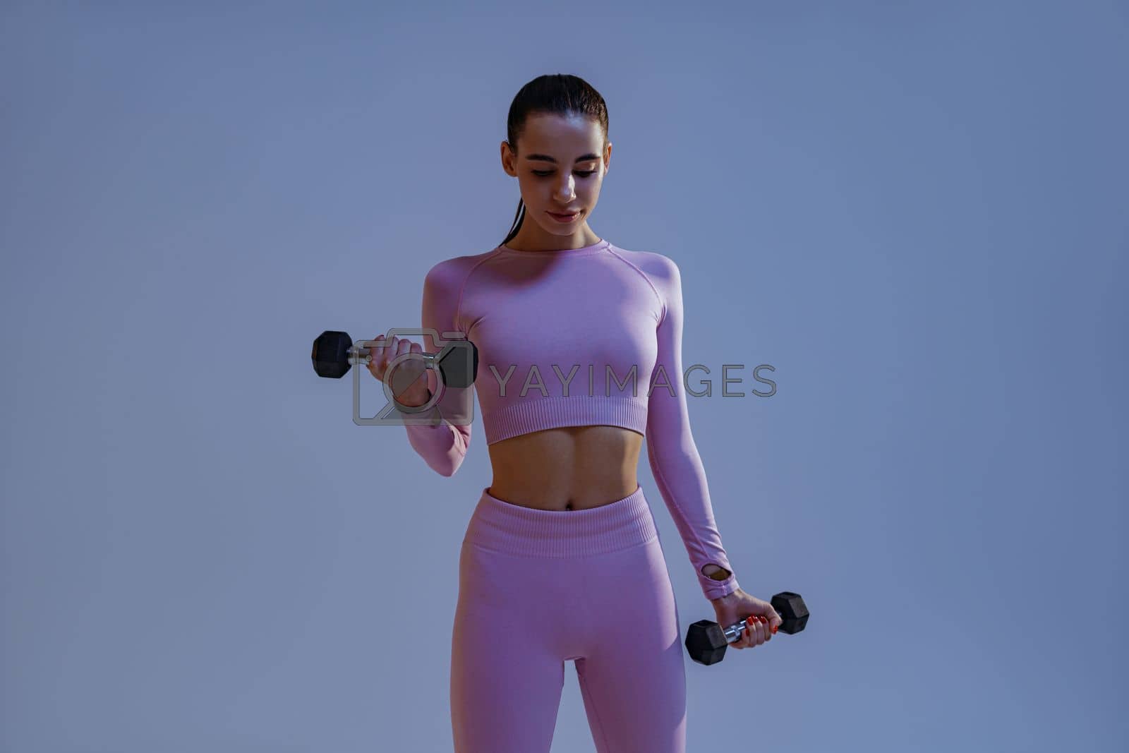 Royalty free image of Fitness woman doing exercises with dumbbells on studio background. Strength and motivation by Yaroslav_astakhov