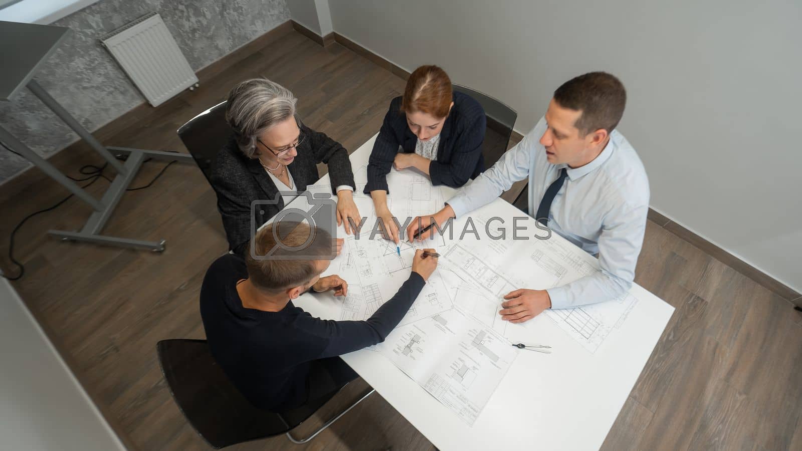 Royalty free image of Top view of 4 business people sitting at a table and discussing blueprints. Designers engineers at a meeting. by mrwed54