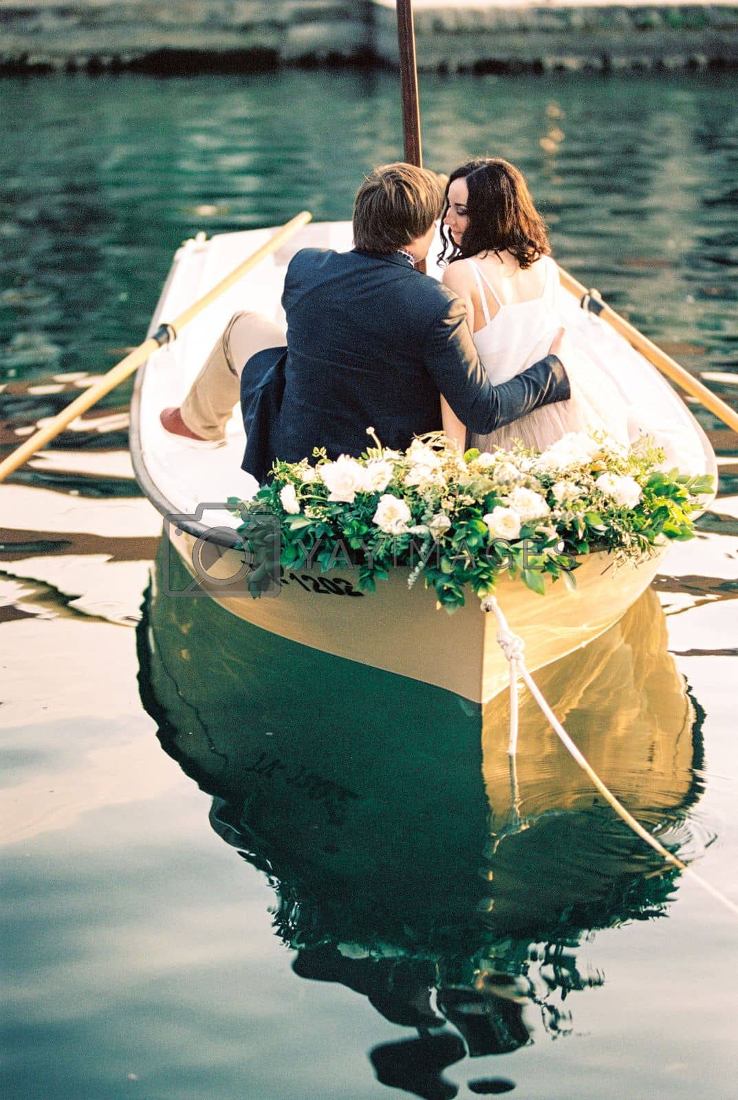 Royalty free image of Man and woman hug and almost kiss in a boat decorated with flowers by Nadtochiy