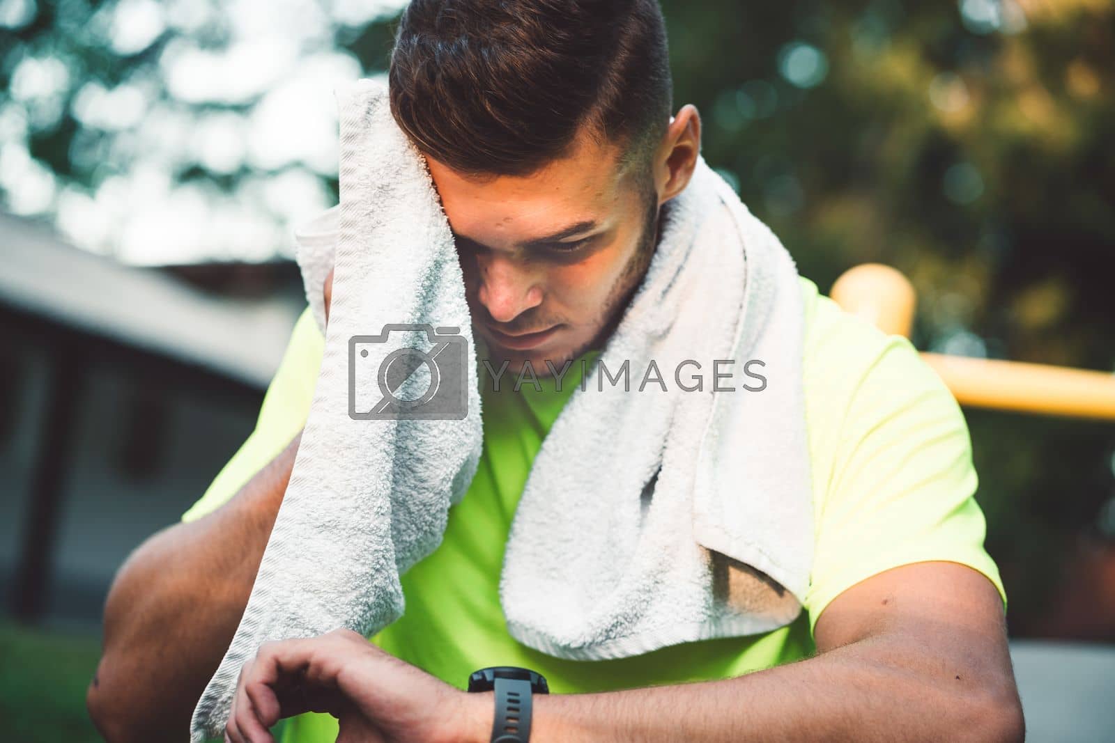 Royalty free image of Sweaty fit man wiping him self with a towel after a workout while looking at his watch by VisualProductions