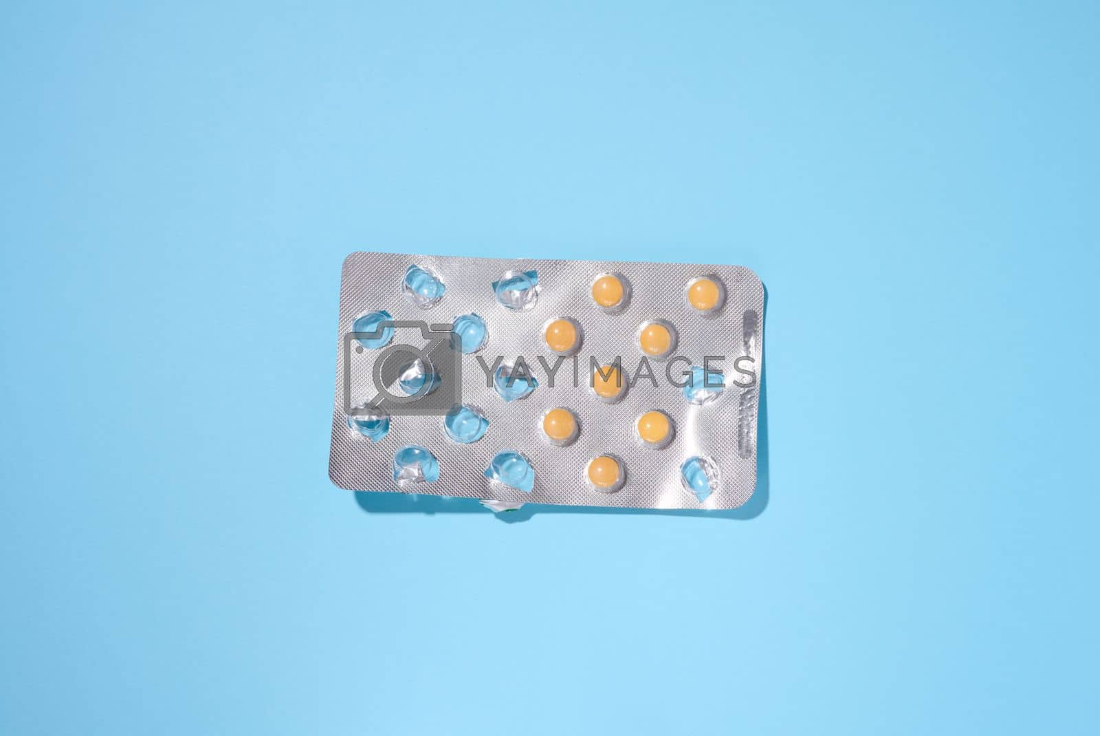Royalty free image of Round yellow pills in a blister pack on a blue background, top view by ndanko