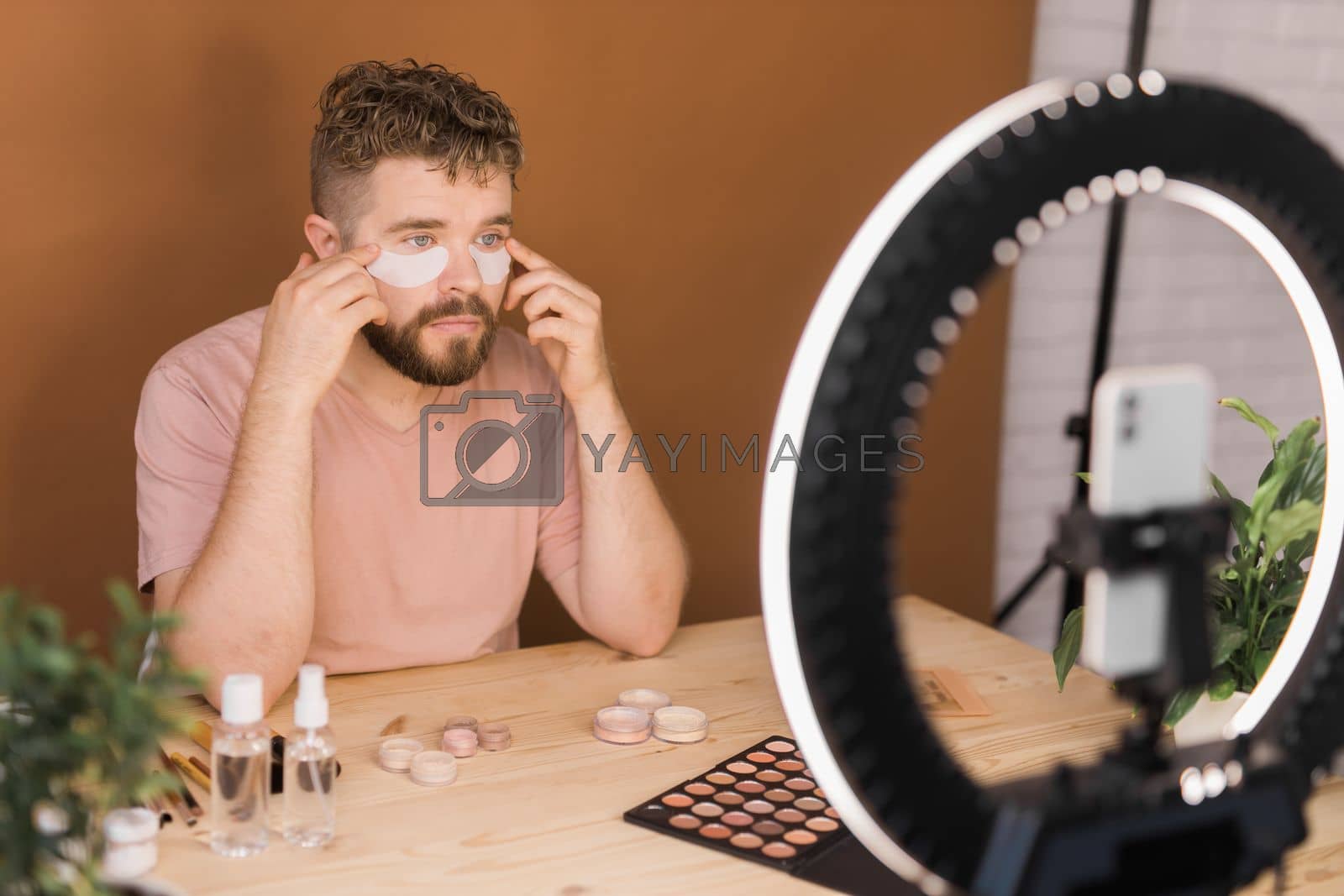 Royalty free image of Man recording video vlog while applying cosmetics or explore cosmetic product. Guy making tutorial make-up for his blog on cosmetics. by Satura86