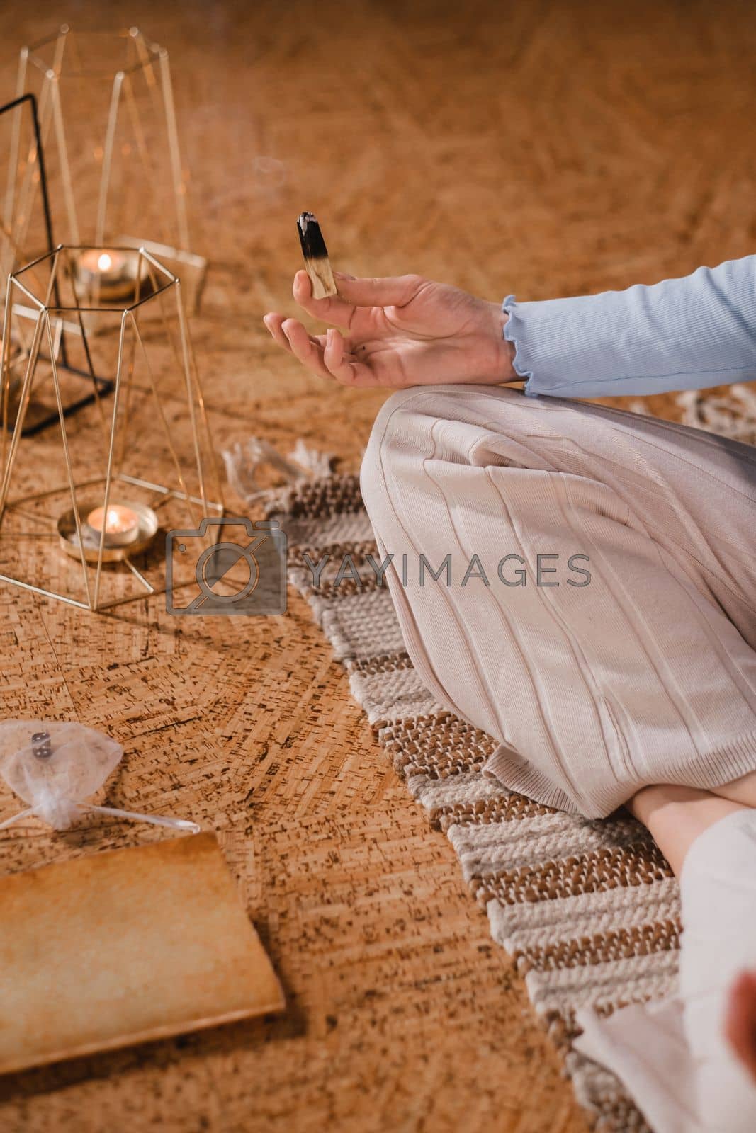 Royalty free image of A woman is sitting in a lotus position with scented candles in her hands in the gym by Lobachad