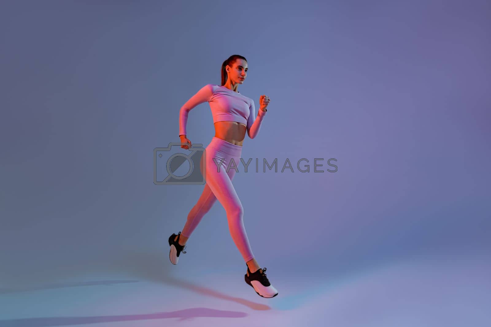 Royalty free image of Pretty sporty woman running in Mid-Air exercising during cardio workout over studio background by Yaroslav_astakhov