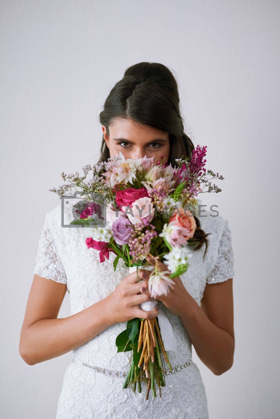 Royalty free image of Ill remember this scent forever. Studio portrait of a young bride holding a bunch of flowers against a gray background. by YuriArcurs