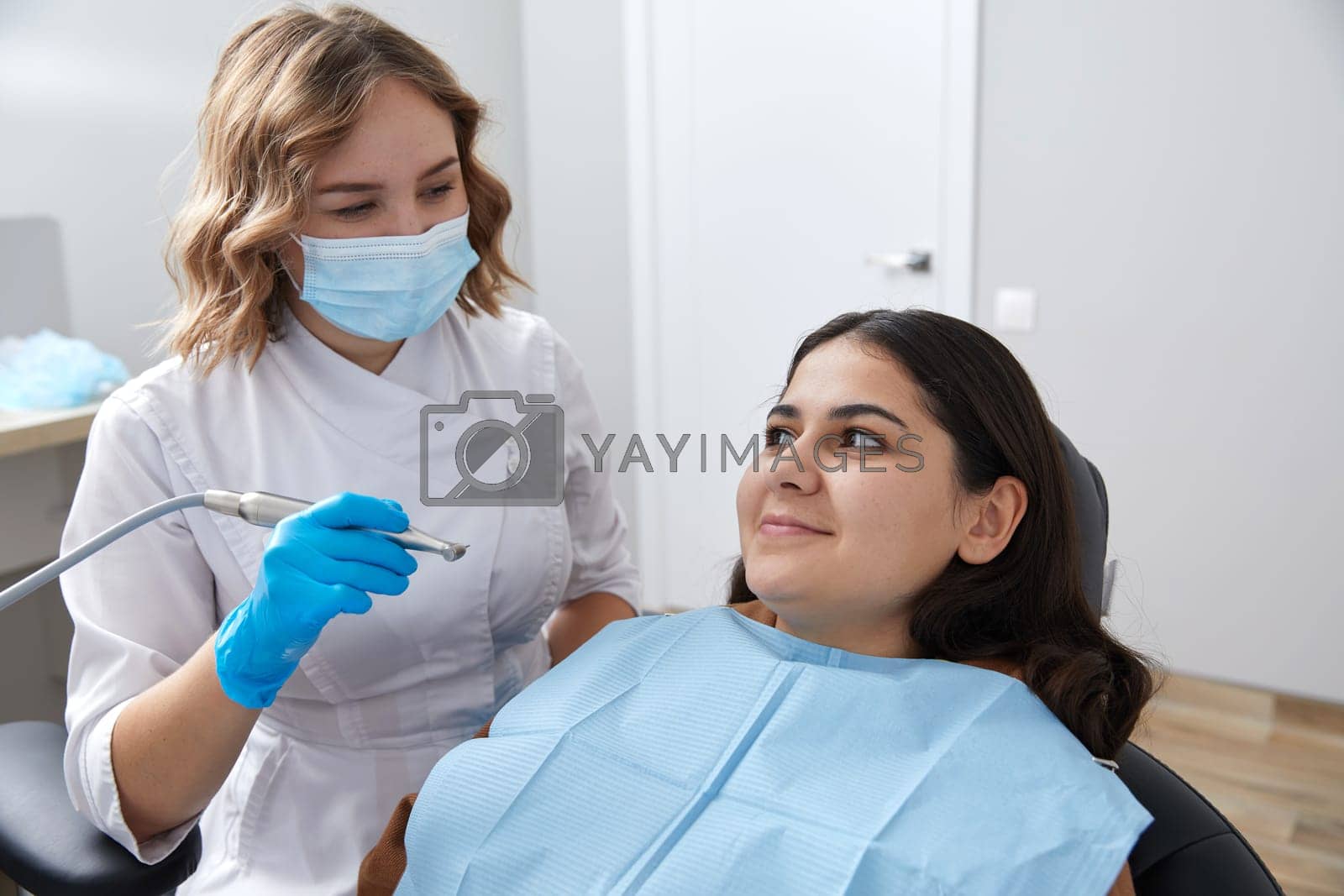 Royalty free image of Dentist drilling tooth of female patient in dental chair by Mariakray