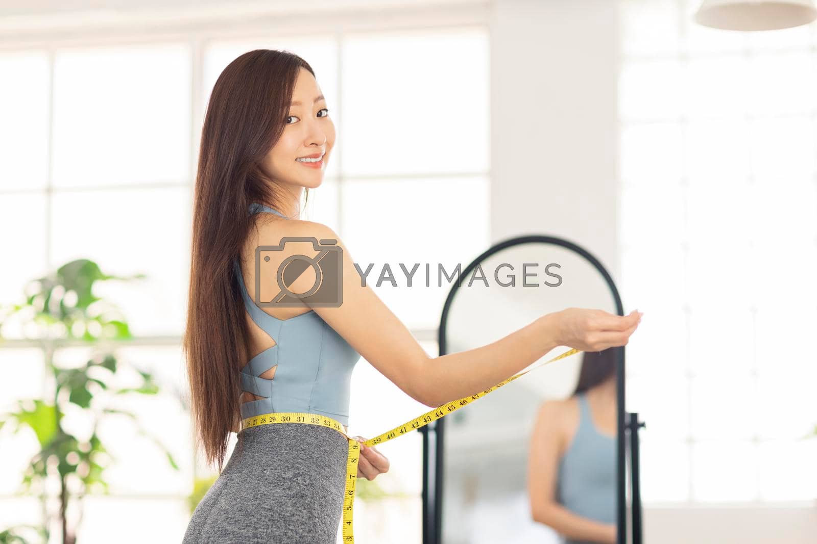 Royalty free image of Young woman measuring waist with tape in front of mirror.Weight loss concept by tomwang