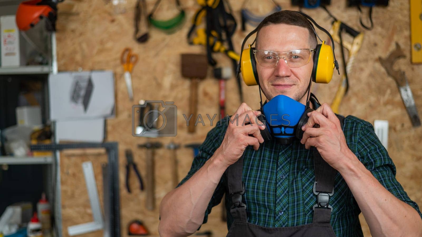 Royalty free image of A carpenter in goggles and earmuffs removes a protective respirator. by mrwed54